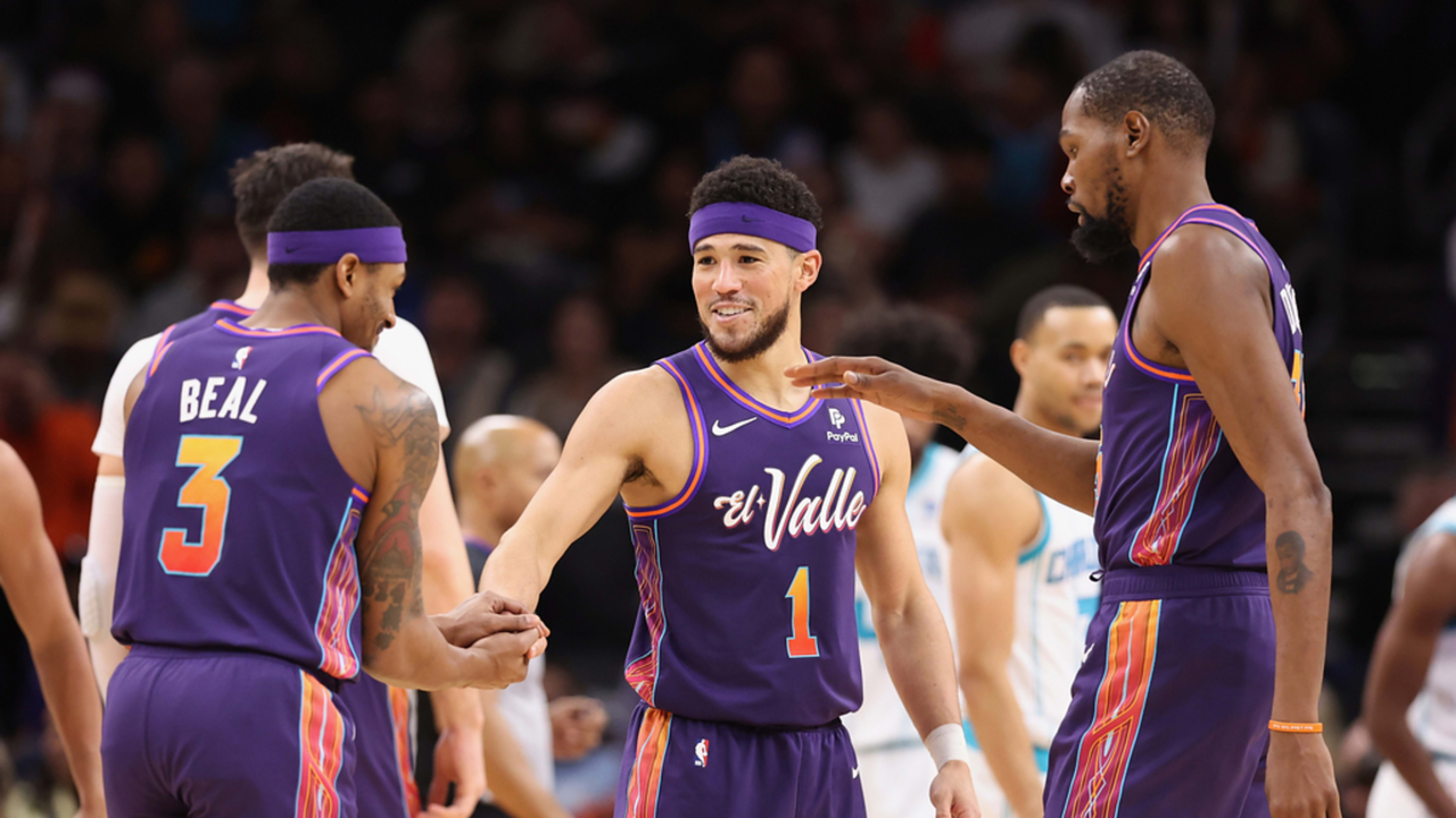 Phoenix Suns players on court in a huddle, exchanging fist bumps and gestures of teamwork