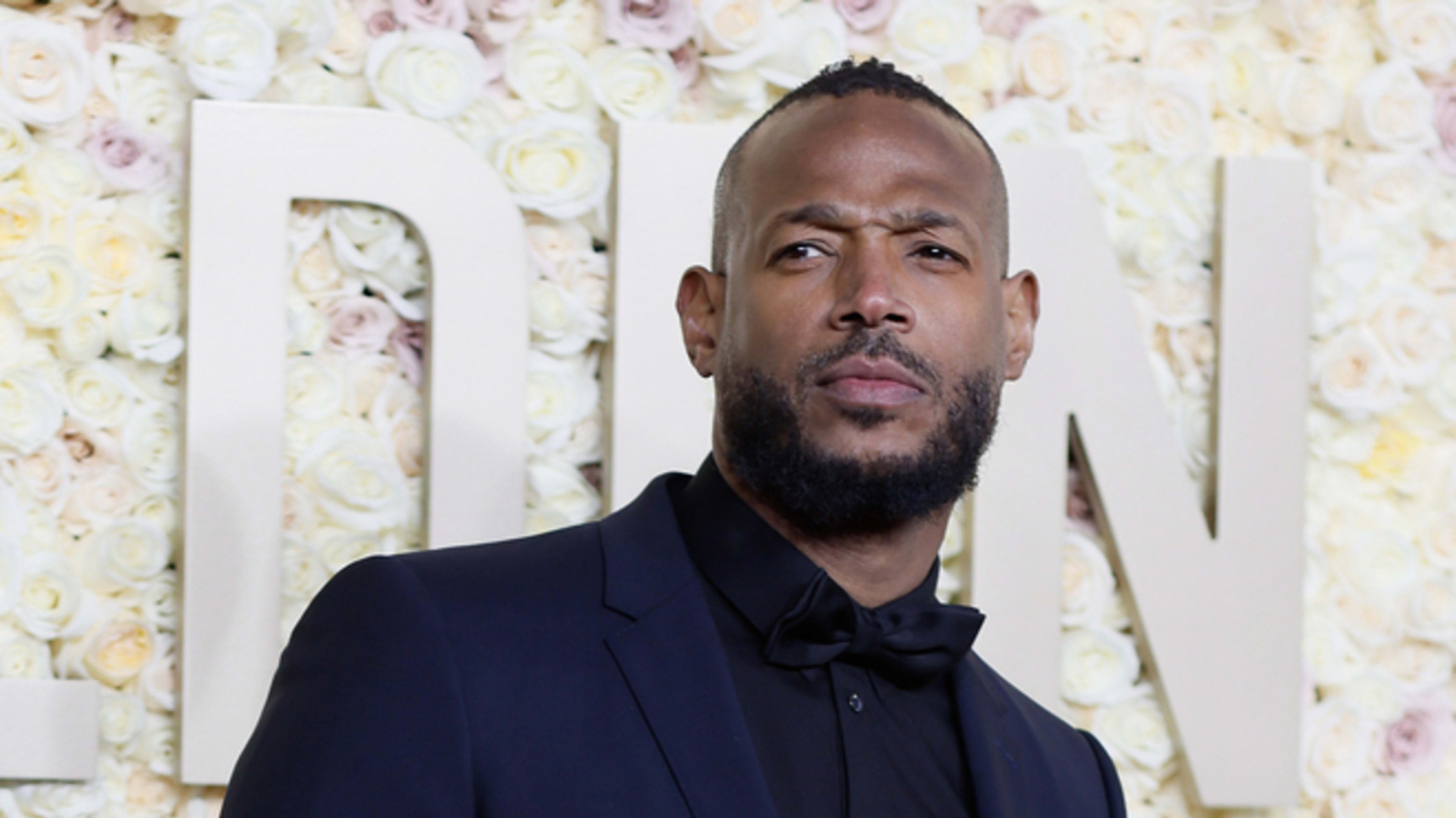 Person in a dark suit posing against a floral background with 'Golden Globes' text