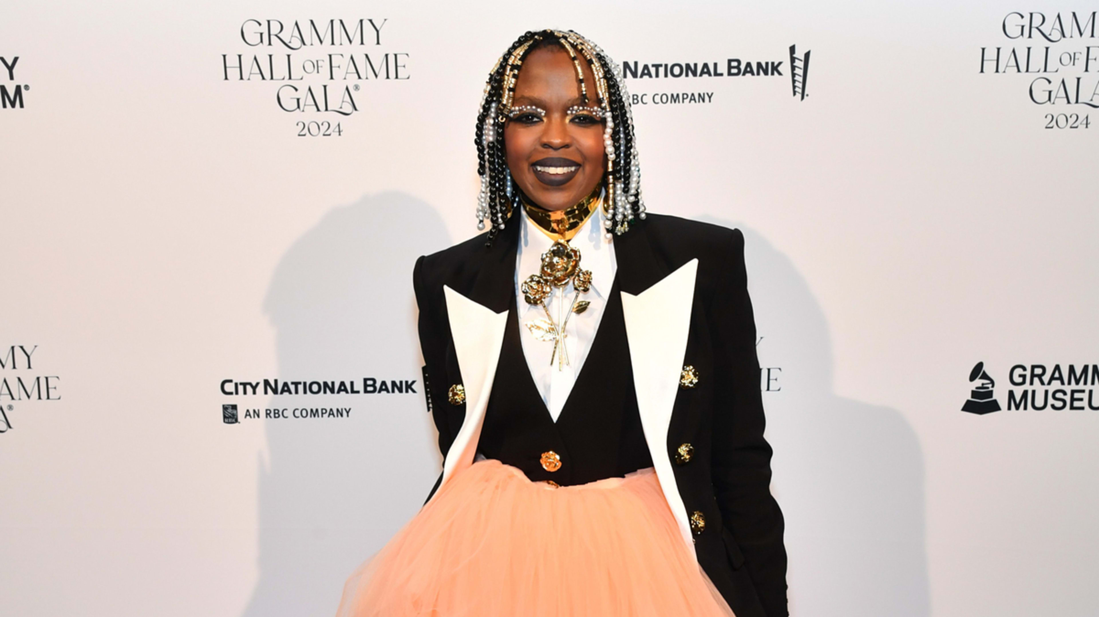 Lauryn Hill at the 2024 Grammy Hall of Fame Gala wearing a black blazer with white lapels, gold jewelry, and a voluminous peach-colored skirt