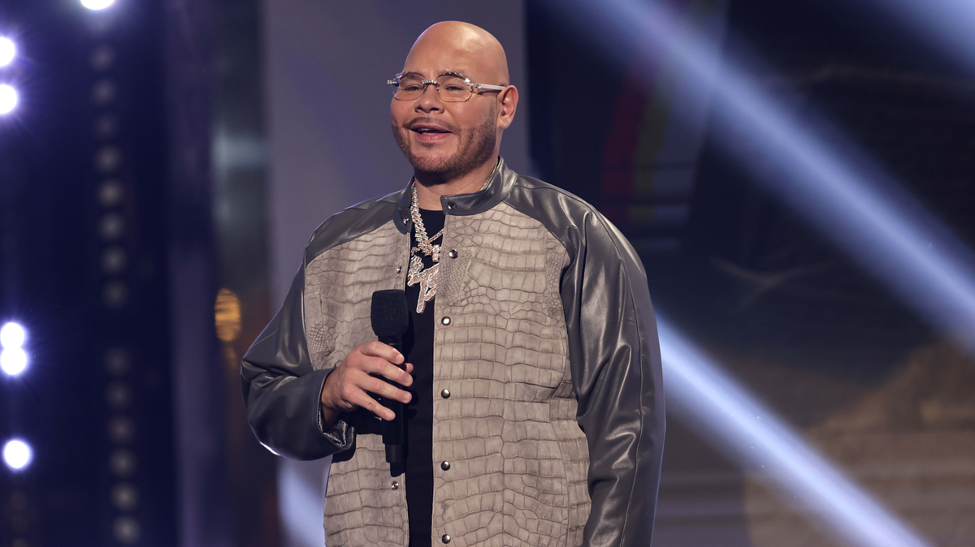 Man on stage in a patterned jacket and shirt, holding a microphone