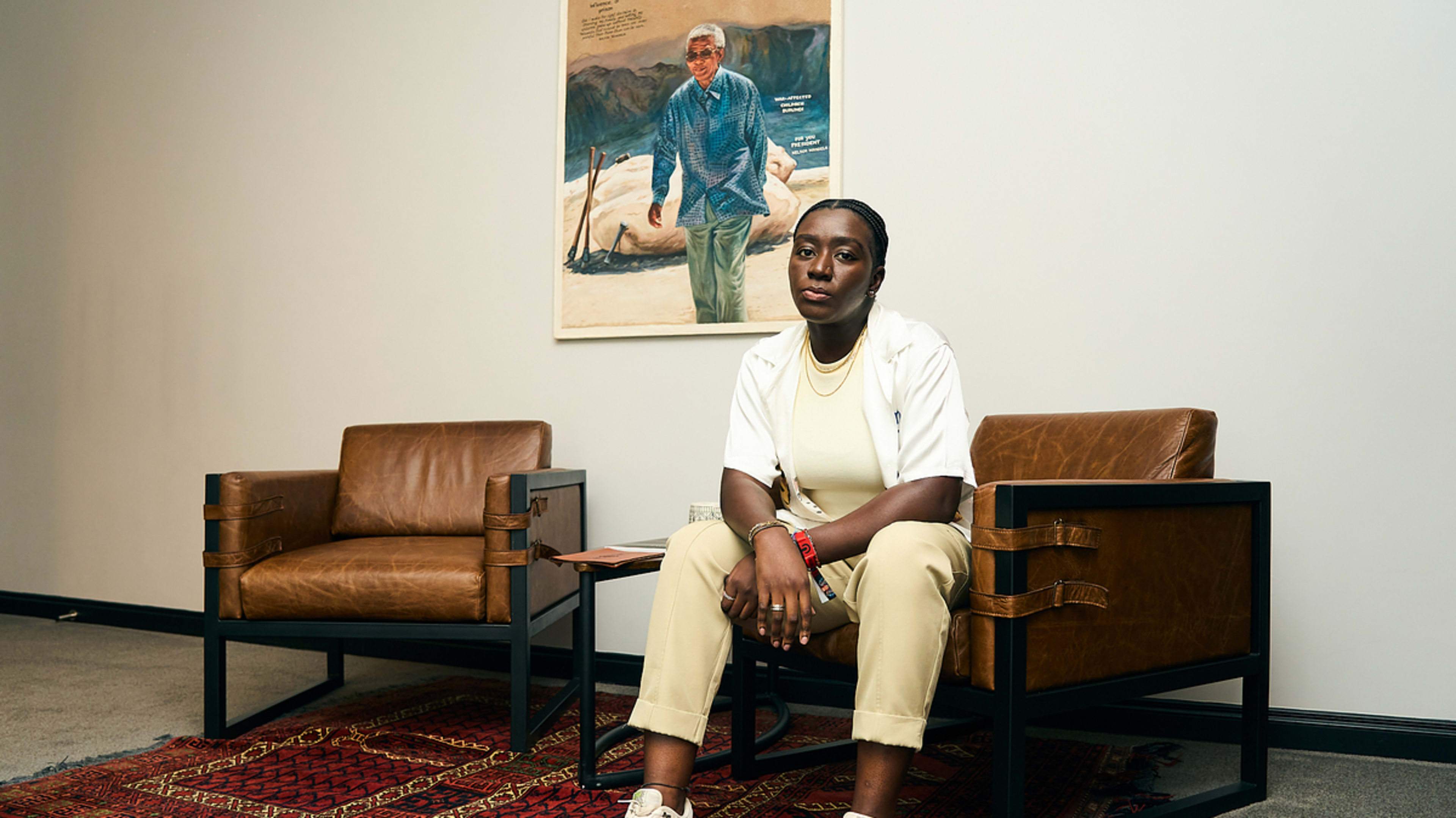 Person seated, casual attire, in front of a portrait on a wall, in a contemplative pose