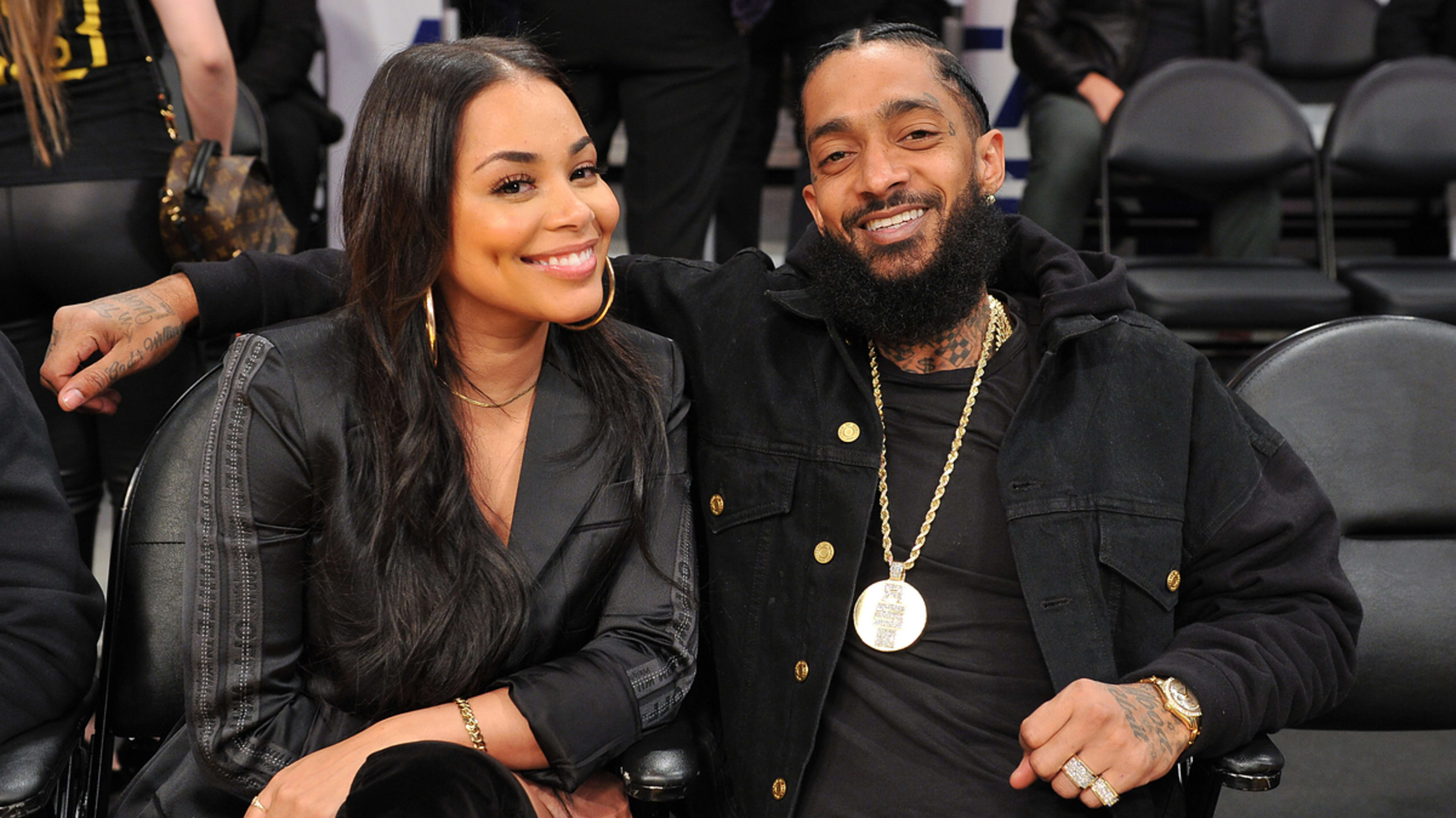 Lauren London and Nipsey Hussle smiling, seated close together at a music event. Both in stylish black attire