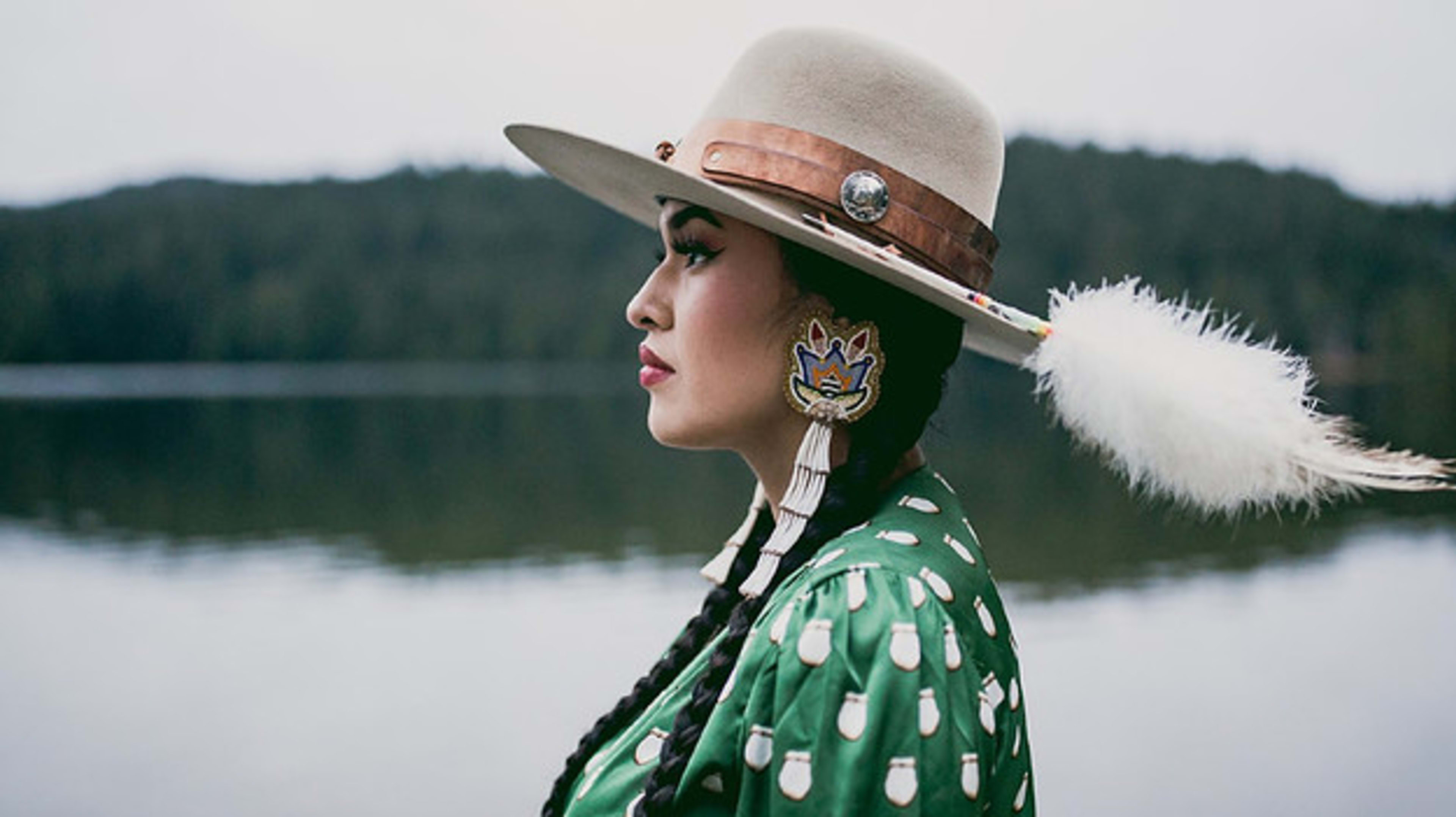 Tia Wood wearing a hat and beadwork earrings, looking to the left