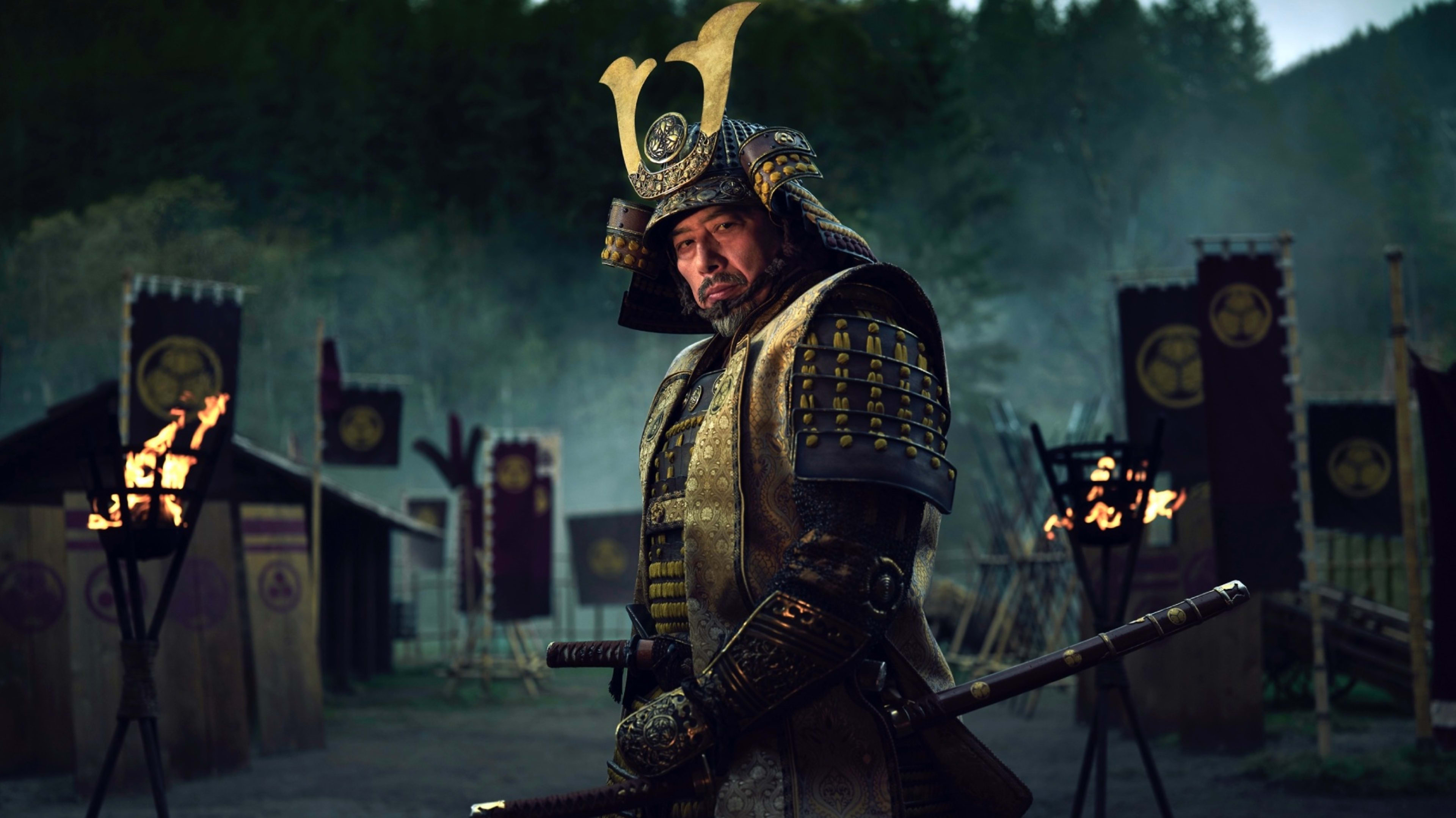 Shogun's Lord Yoshii Toranaga (played by Hiroyuki Sanada) stands in the middle of a war encampment wearing armor and his sword.