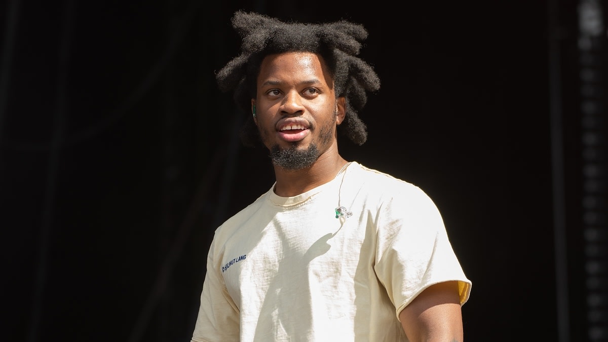 Denzel Curry performs on stage wearing a light shirt, ear monitors, and rocking a natural hairstyle