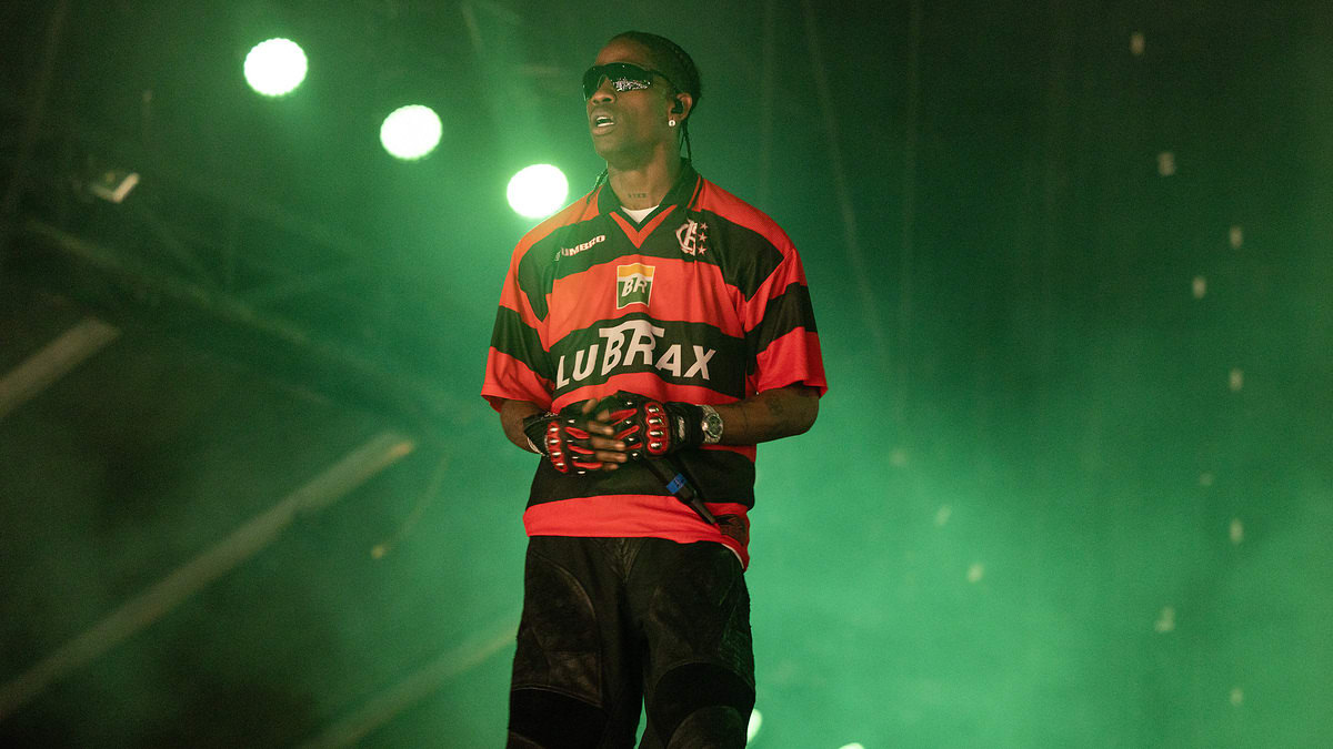 A person wearing a red and black sports jersey, black shorts, and black gloves performs on stage under green lights