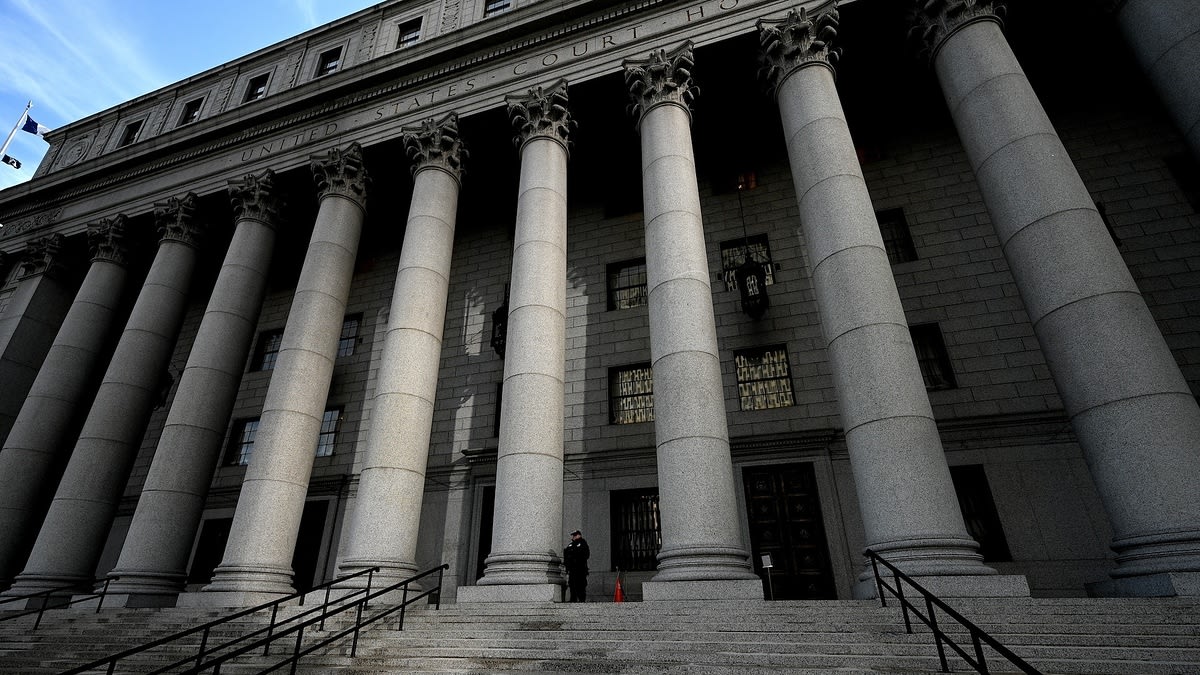 A person stands alone on the steps of a large courthouse with tall columns. The building's facade reads "United States Court House."