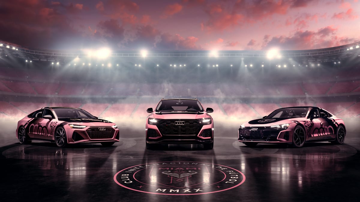 Three customized Audi vehicles with a black and pink gradient design are showcased on a foggy stadium field at night