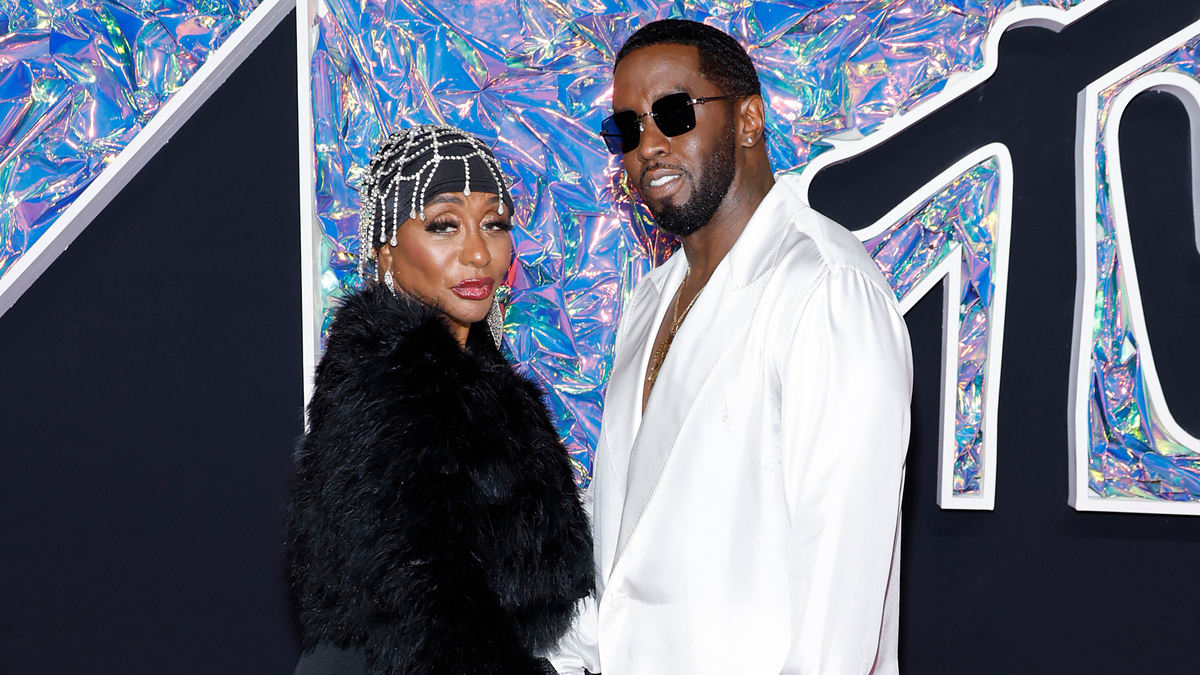 Janice in a fur shawl stands with Sean "Diddy" Combs in a white suit and sunglasses at a music event