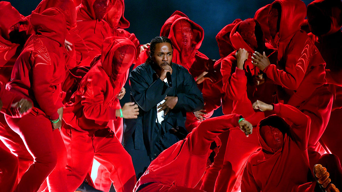 Kendrick Lamar performs surrounded by a group of dancers in identical hooded outfits with covered faces during a dynamic stage show