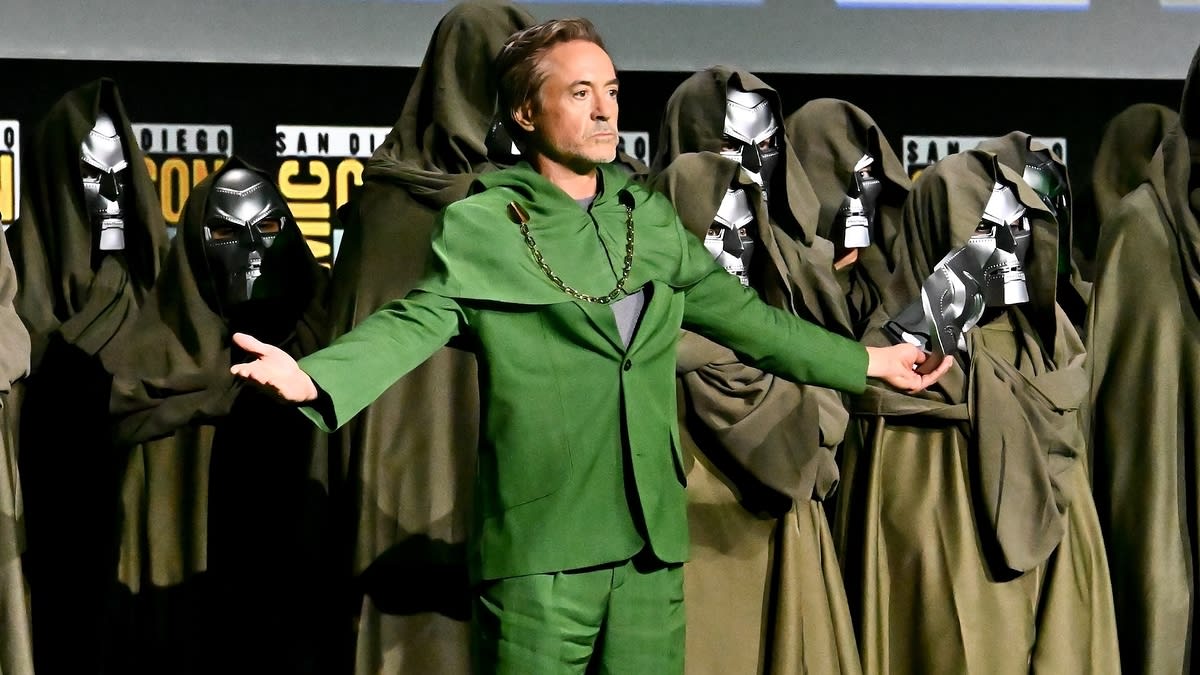 Robert Downey Jr. dressed in a green suit stands among people in hooded cloaks and metallic masks at San Diego Comic-Con