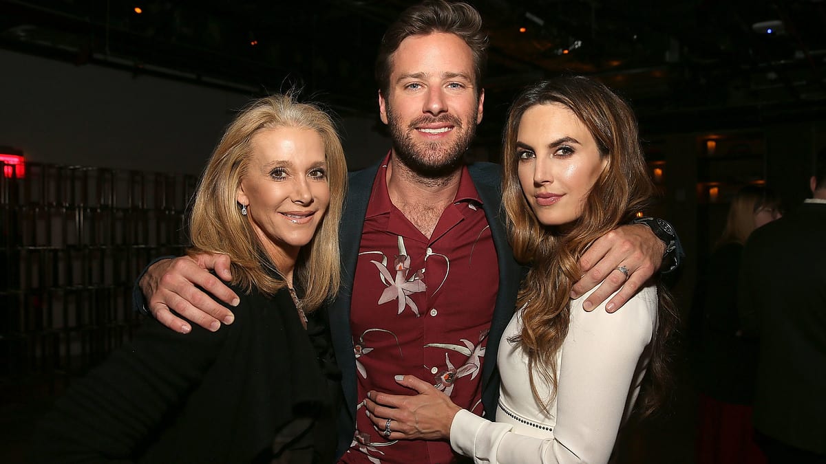 Elizabeth Chambers and Armie Hammer, in stylish casual outfits, pose together with an older woman at an indoor event