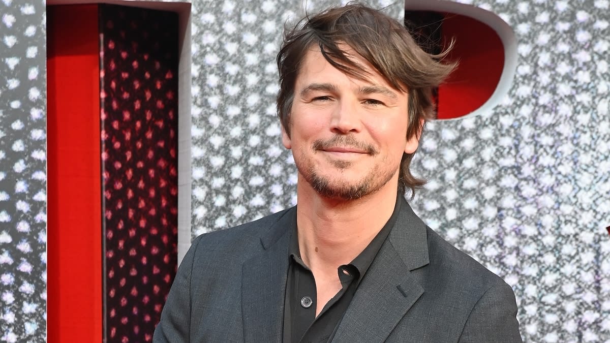 Josh Hartnett smiling at a red carpet event, wearing a dark suit and a black shirt