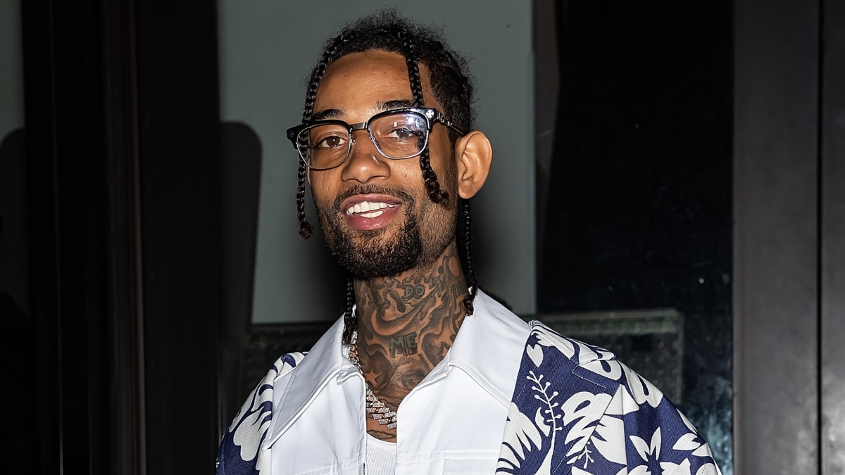 PnB Rock wearing glasses and a floral-patterned jacket at a night event, smiling for the camera