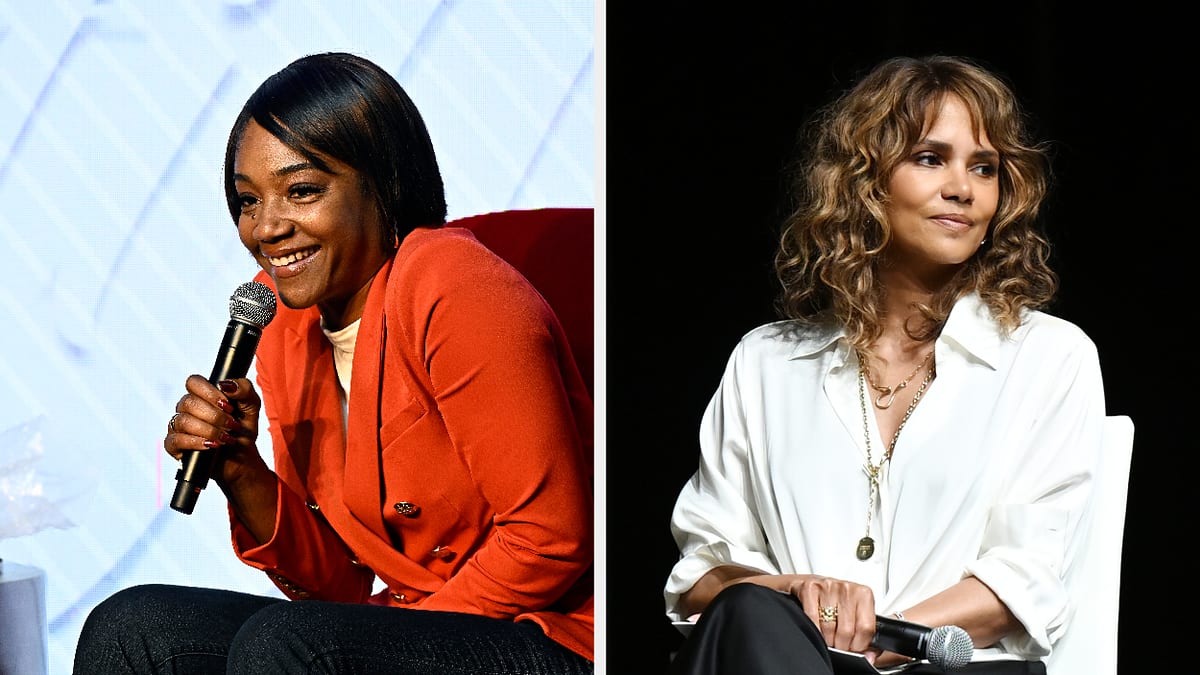 Tiffany Haddish, in a stylish red blazer, speaks into a microphone. Halle Berry, with curly hair, wears a white blouse and long necklaces while sitting
