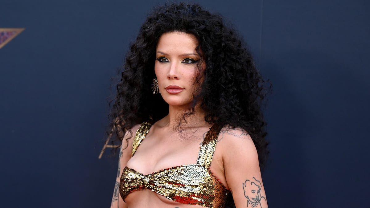 Halsey poses on the red carpet in a shimmering gold top with her curly hair styled loosely. Tattoos on her arms are visible