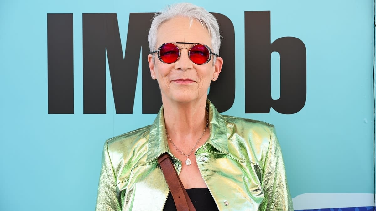 Jamie Lee Curtis wearing a shiny green jacket and red sunglasses at an IMDb event