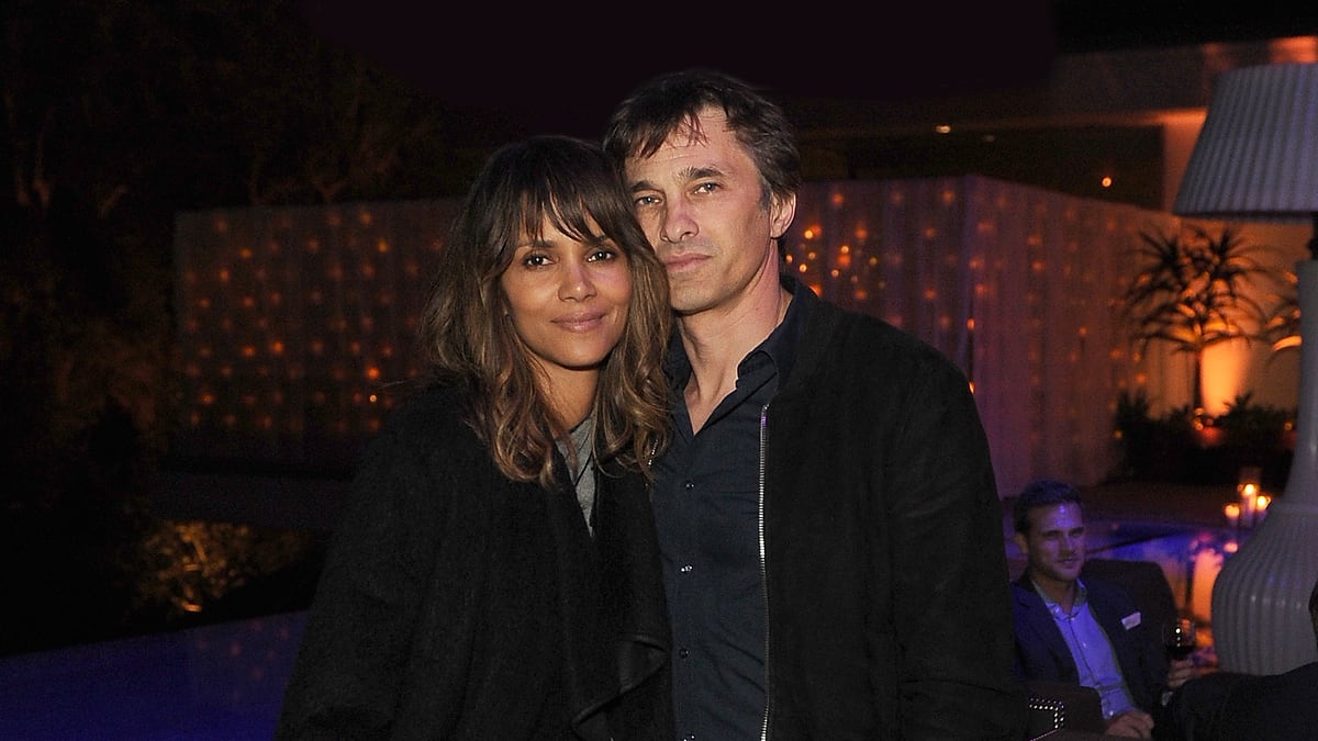 Halle Berry and Olivier Martinez pose together at an evening event. Halle wears a layered, casual outfit with a cardigan and leather pants. Olivier wears a jacket and dark jeans