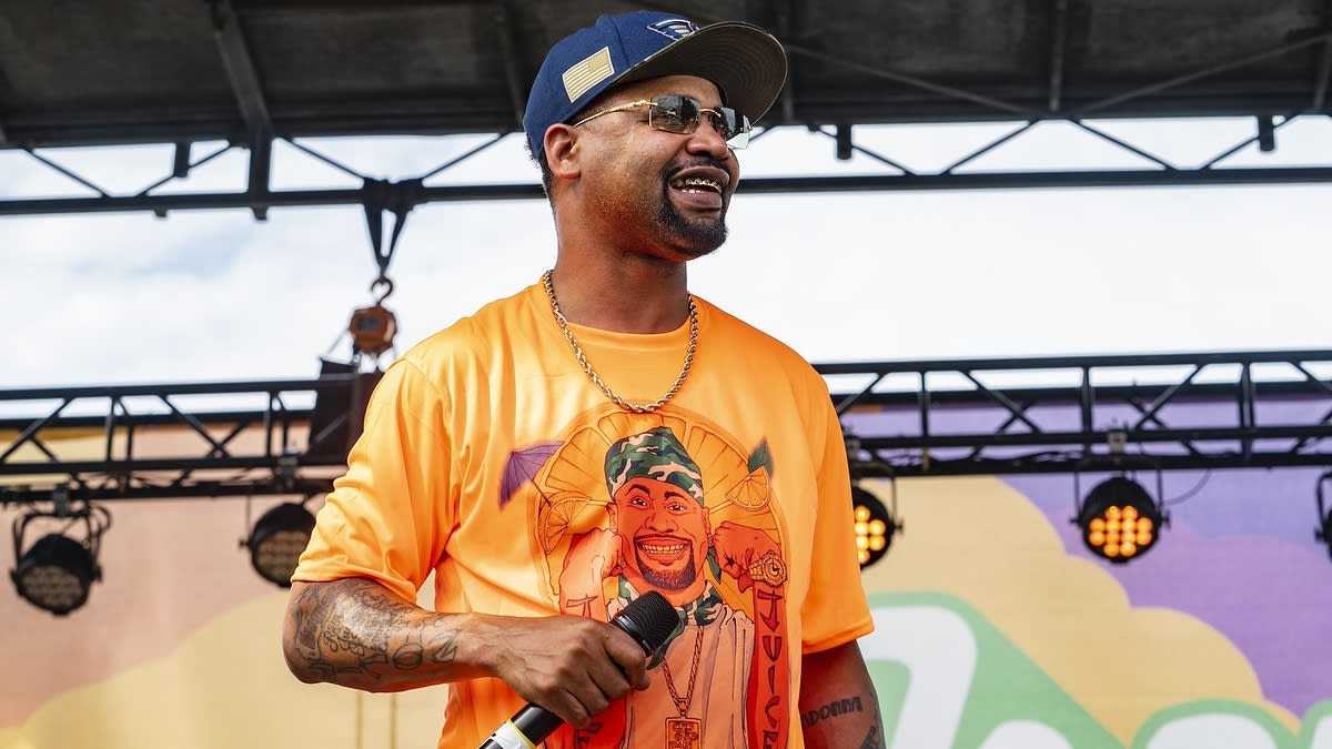 Man in a vibrant graphic T-shirt and cap holds a microphone on stage