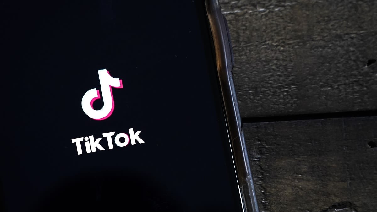 TikTok logo displayed on a smartphone screen resting on a dark wooden surface