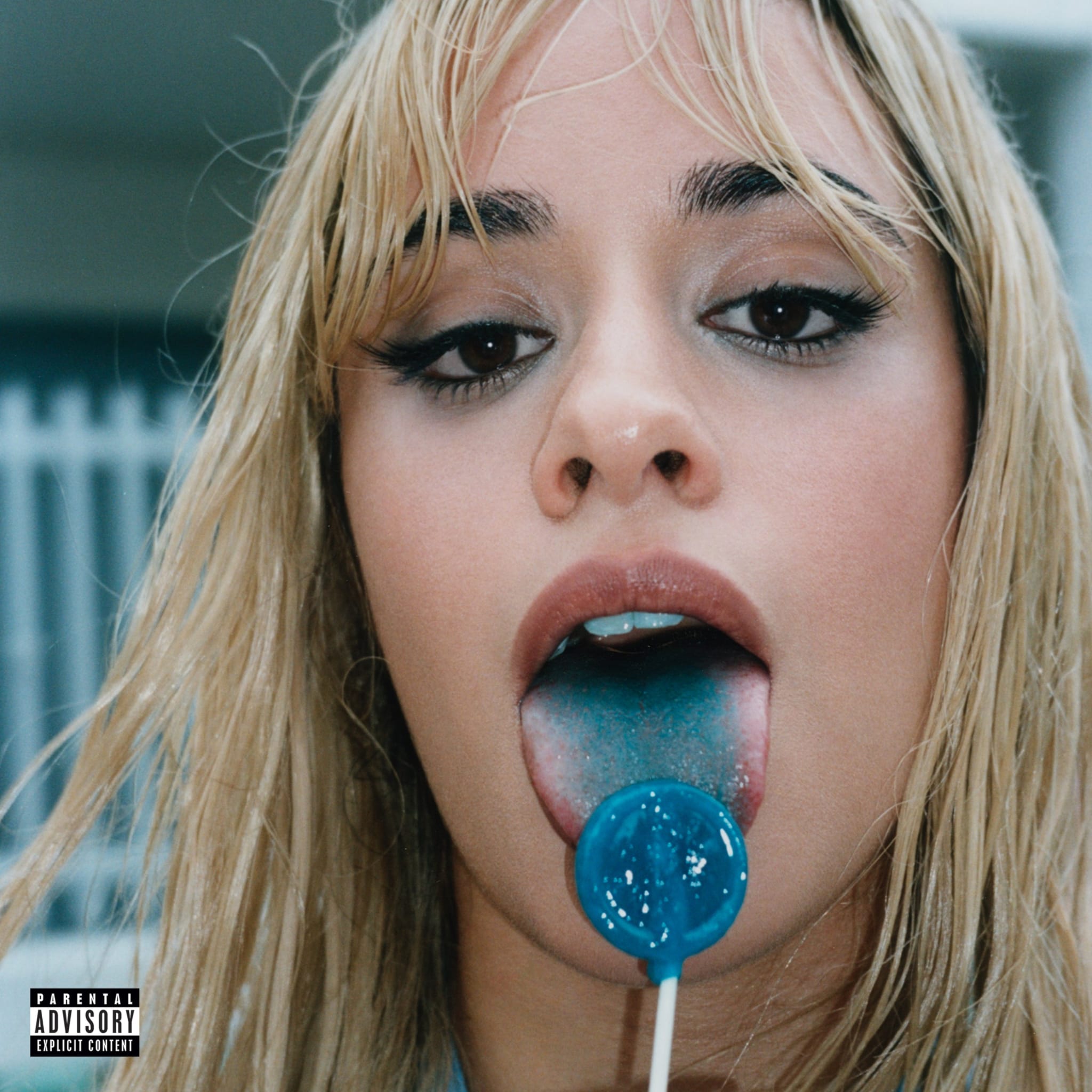 Close-up of singer Camila Cabello licking a blue lollipop, with an explicit content warning in the bottom-left corner