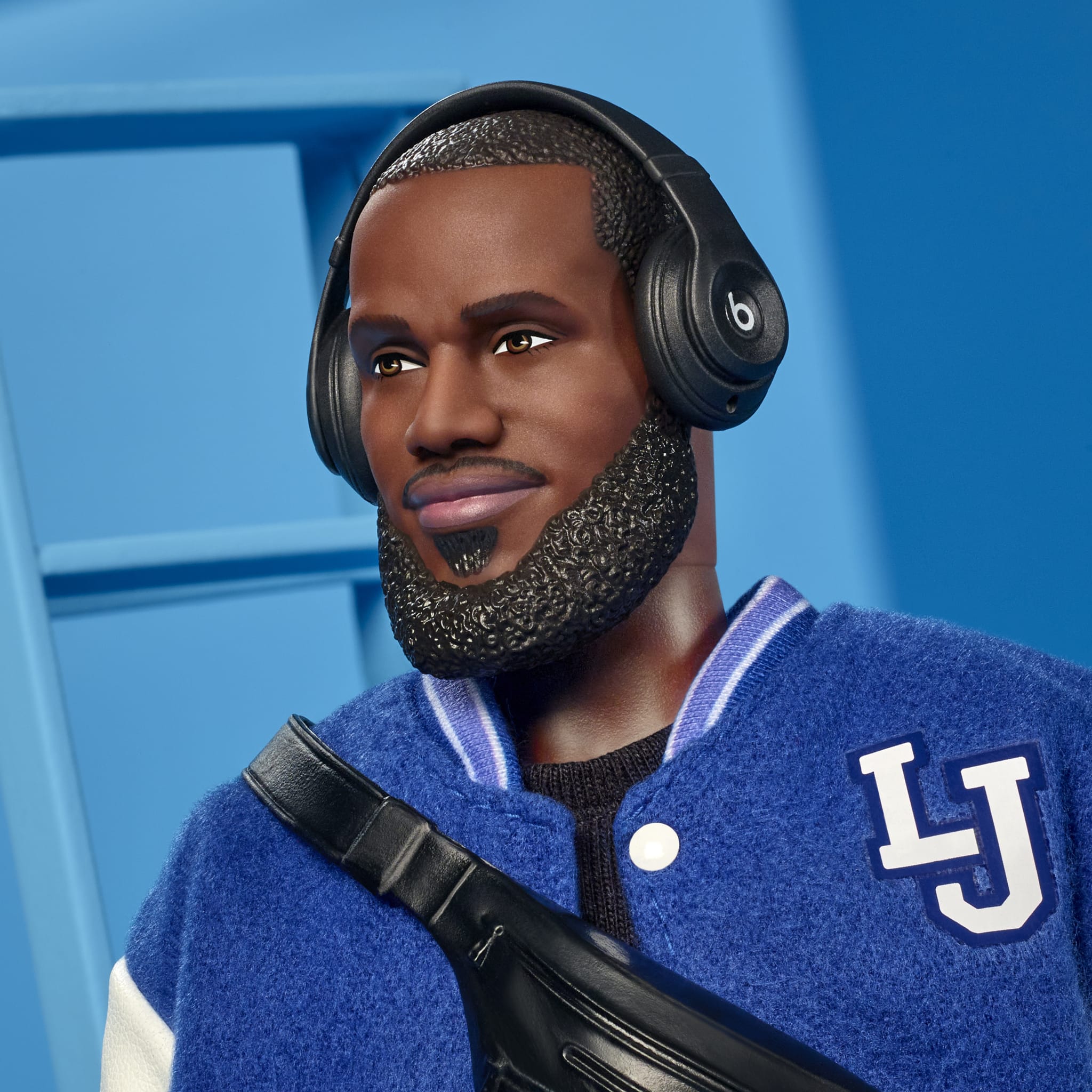 A doll resembling LeBron James wearing Beats headphones, a blue varsity jacket with "LJ" initials, and a black crossbody bag.