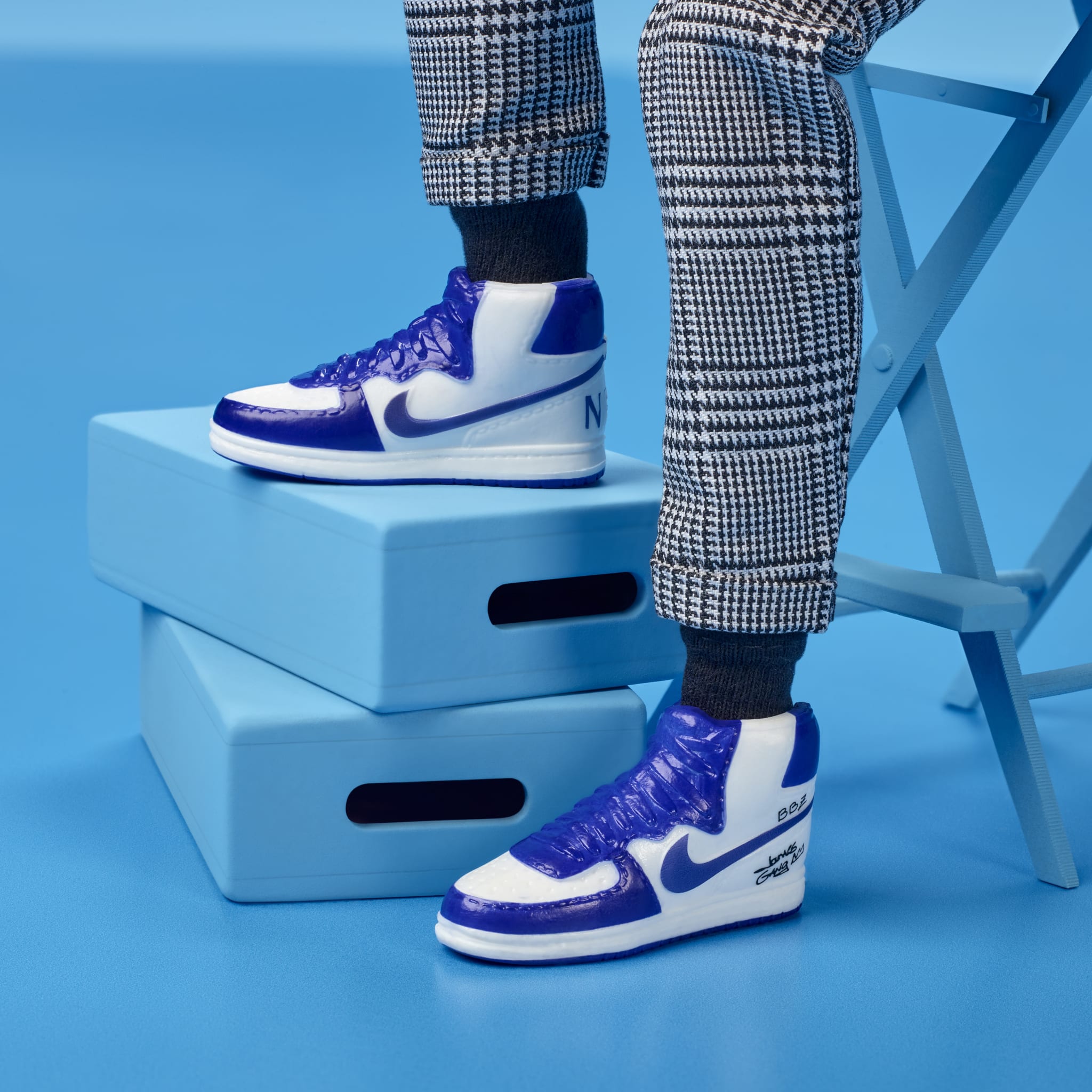 A person wearing blue and white Nike high-top sneakers and checkered pants, standing on blue blocks.