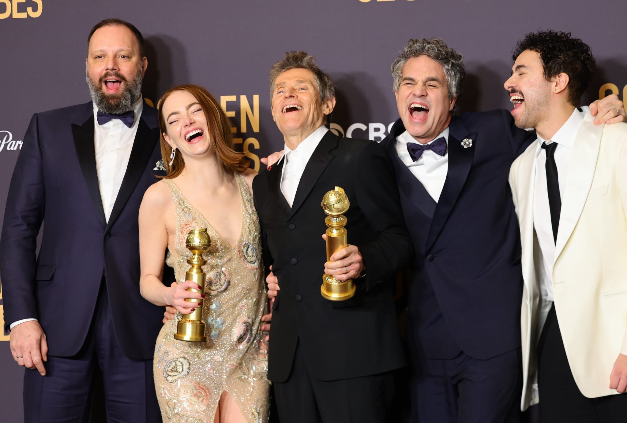 Five actors at the Golden Globes, laughing and holding awards, in formal wear