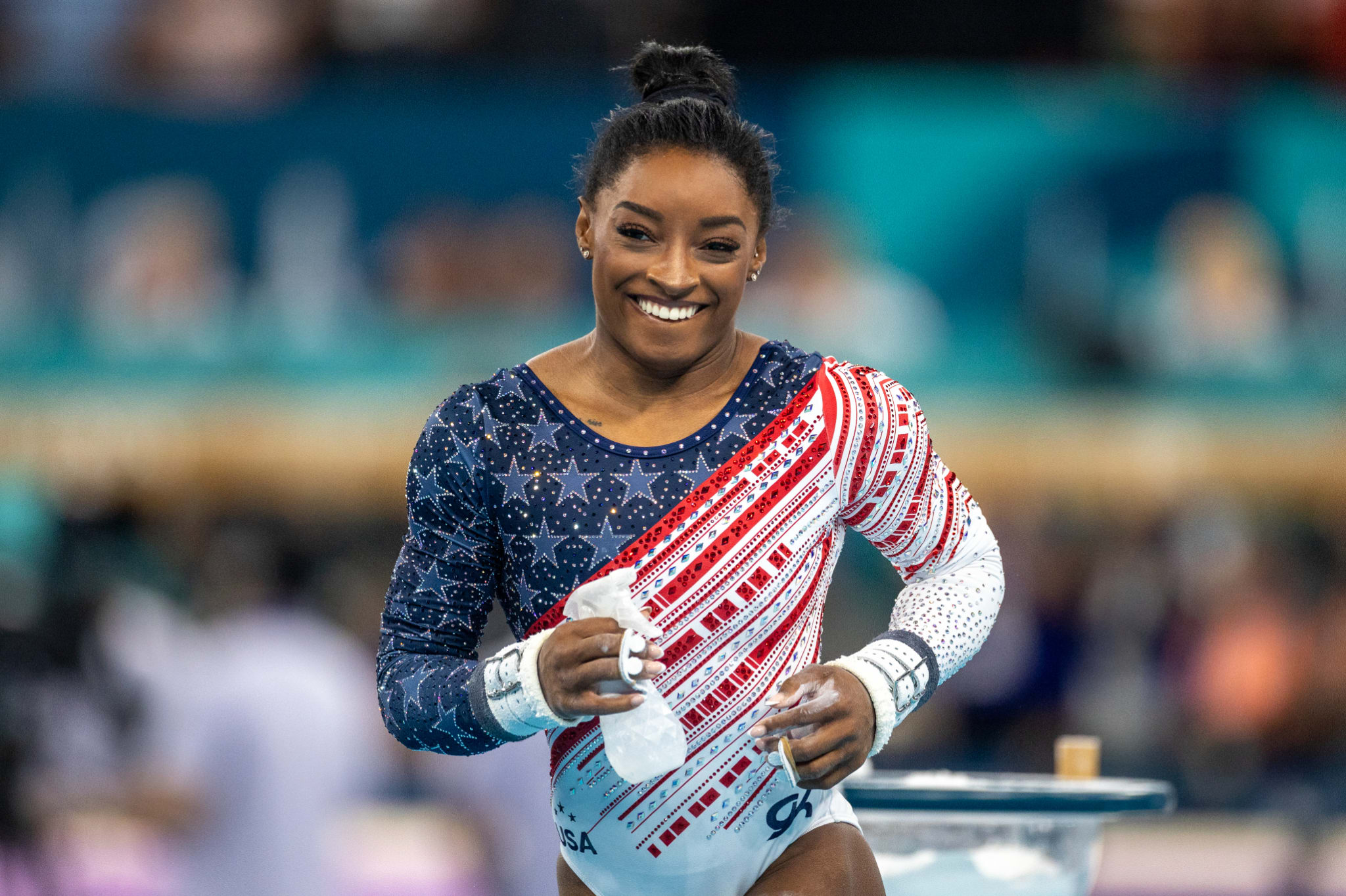 Simone Biles in a gymnastics uniform with stars and stripes, holding chalk at a competition