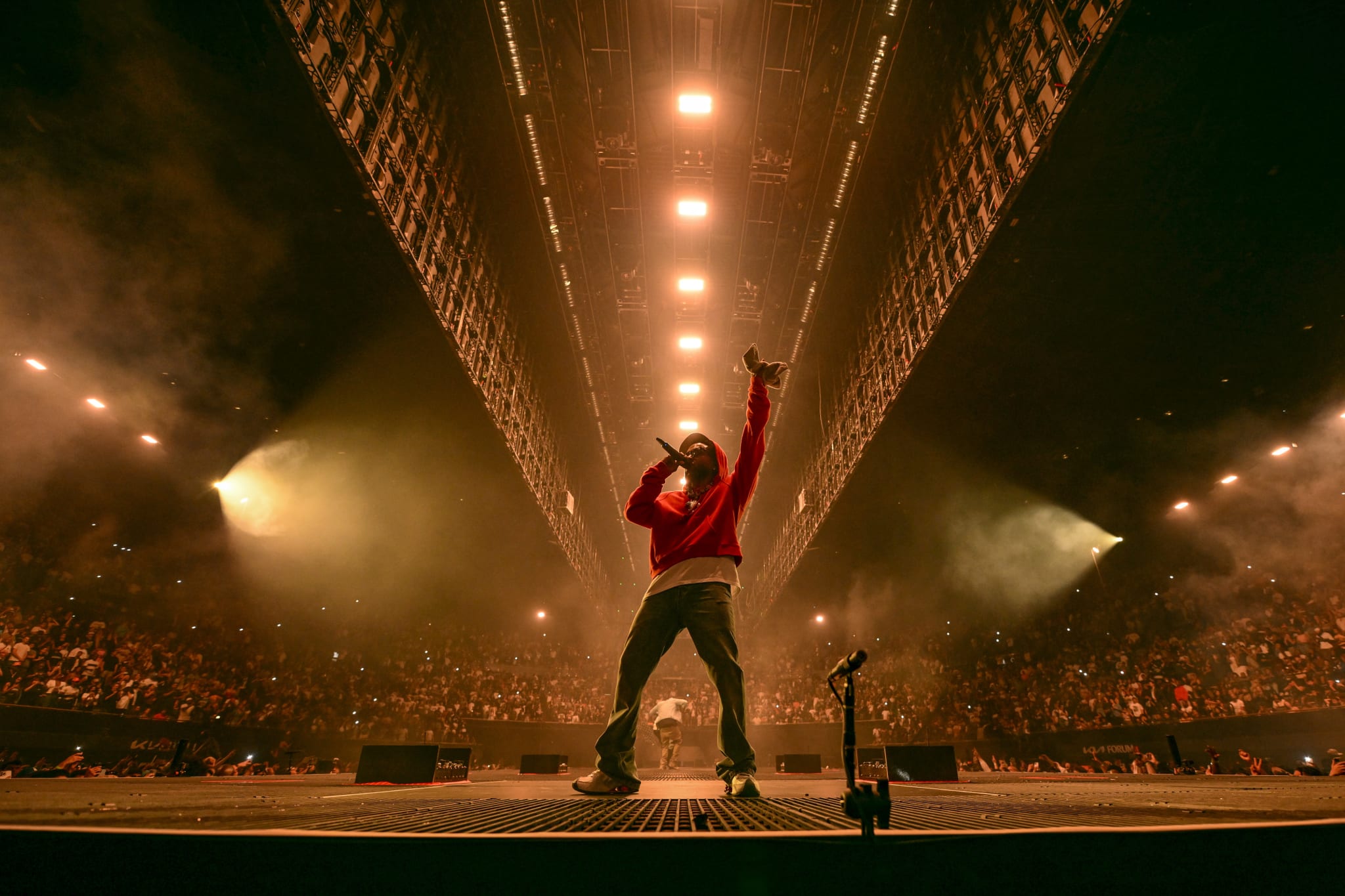 A rapper performs energetically on a stage under bright lights at a packed concert venue