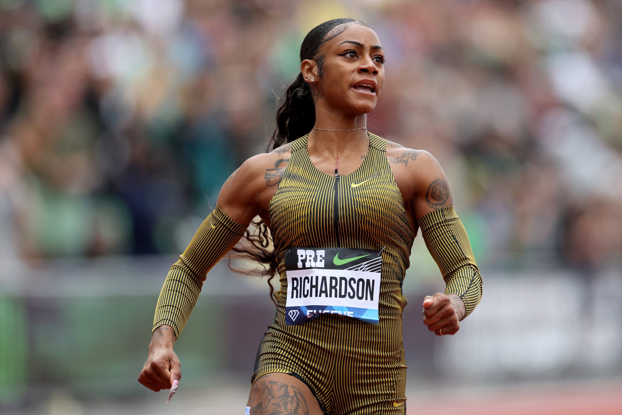 Sha'Carri Richardson sprinting during a track and field event, wearing a fitted athletic suit with long sleeves