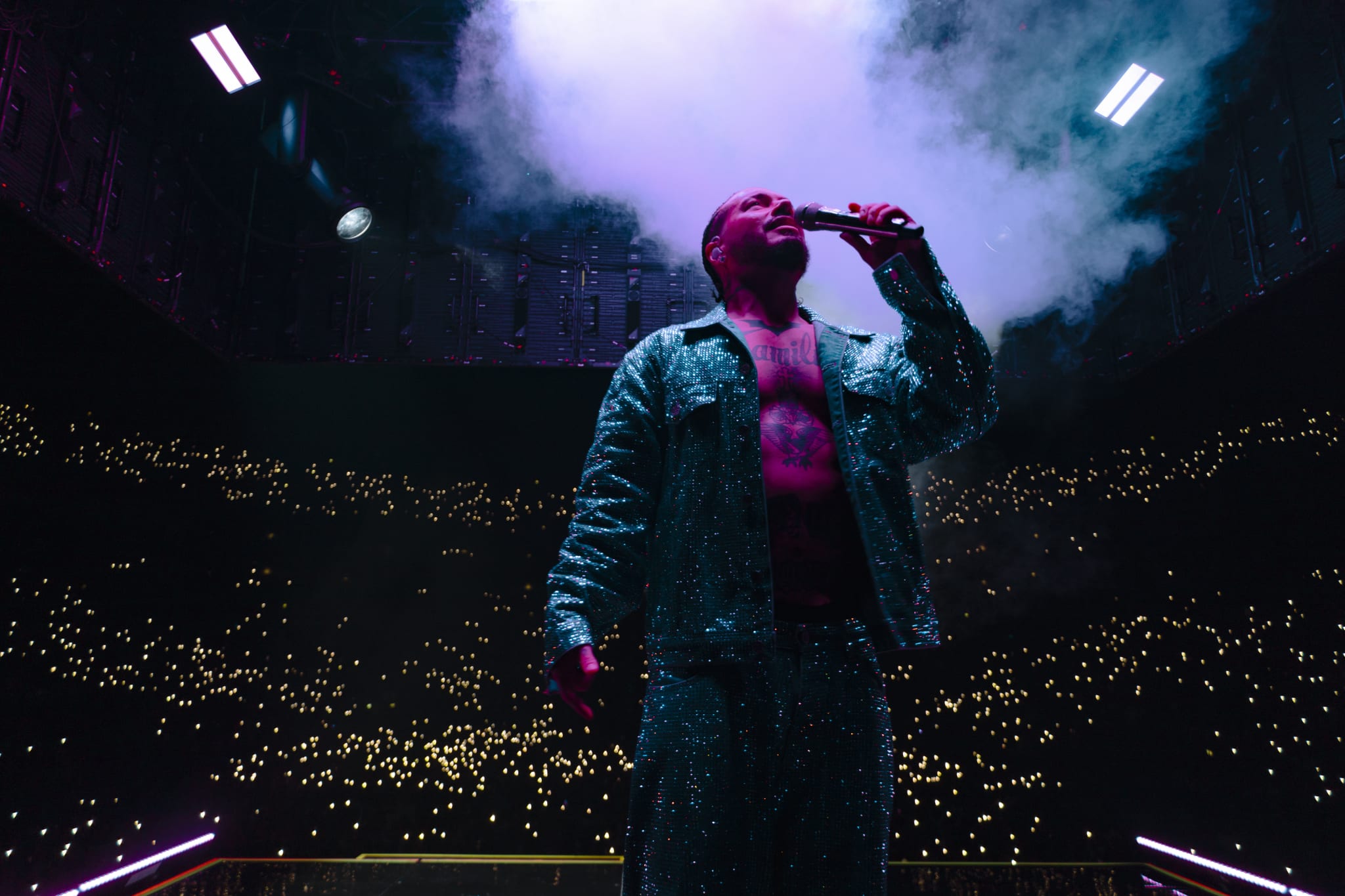 Post Malone performs on stage, illuminated by stage lights and surrounded by a sea of audience lights during a concert