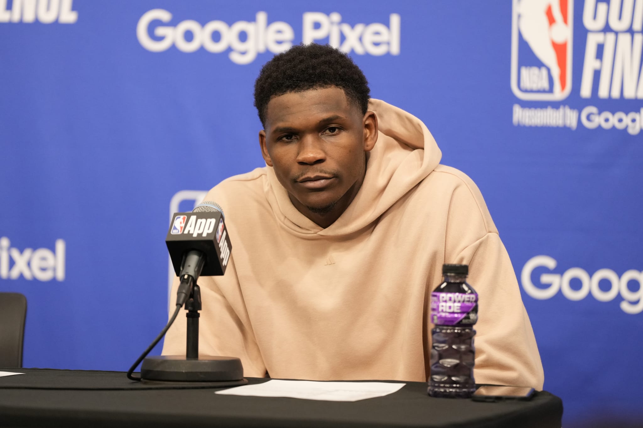 Anthony Edwards speaking at an NBA press conference, wearing a hoodie, with a microphone and a sports drink bottle on the table. Google Pixel branding in the background