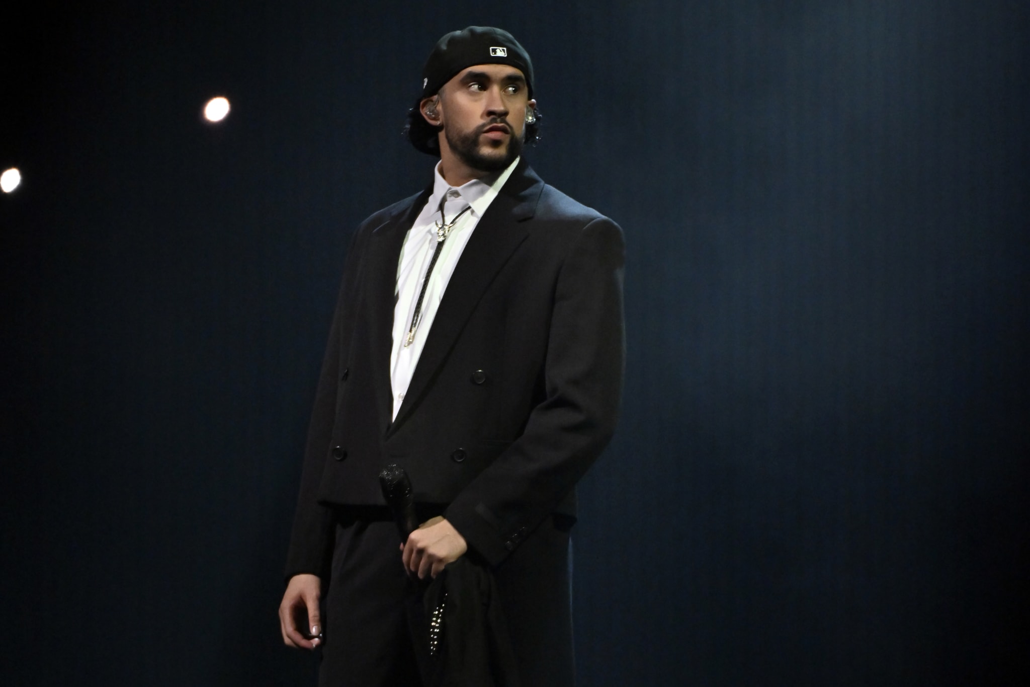 Bad Bunny in suit stands solemnly on stage with spotlight above