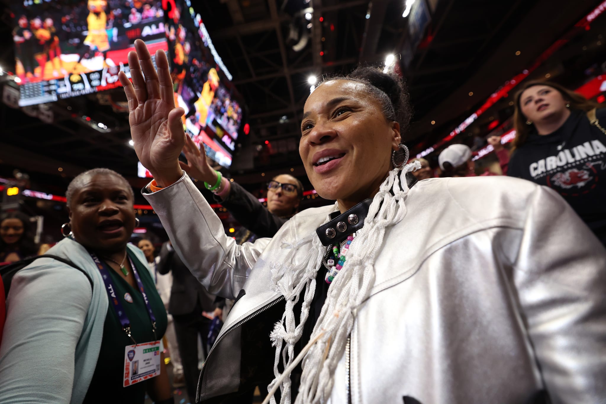 Two people at a sports event, one gesturing excitedly. They are on the sidelines with a crowd in the background