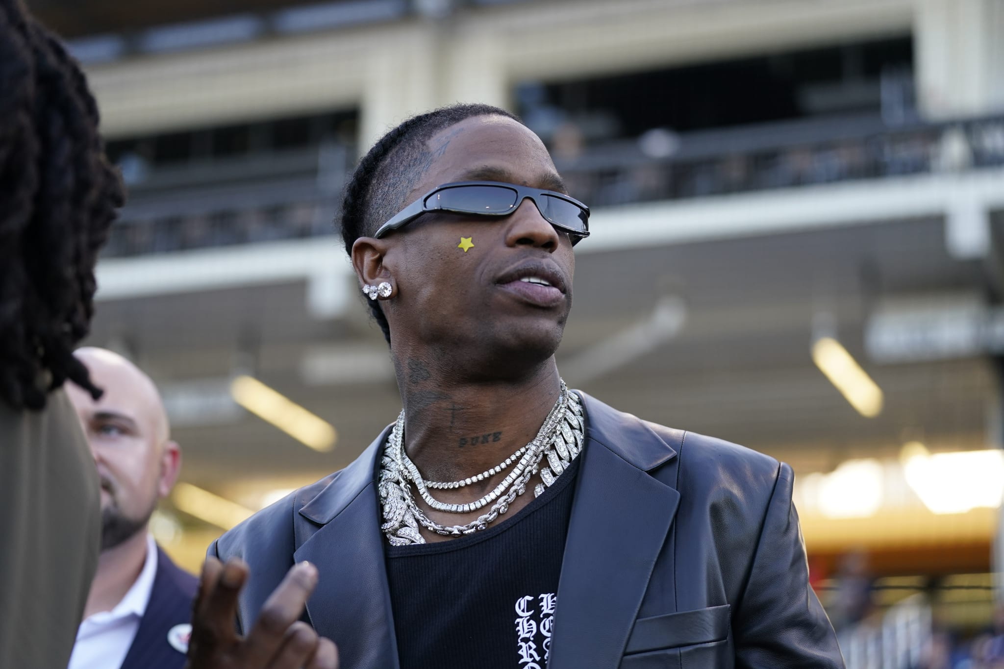 Man in a black suit and sunglasses at an event, with a blurred background