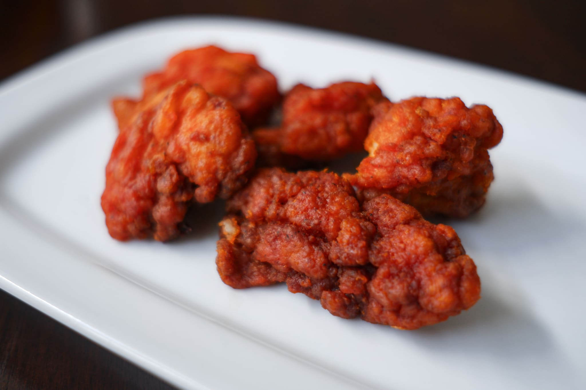 A close-up of several spicy chicken wings on a white rectangular plate