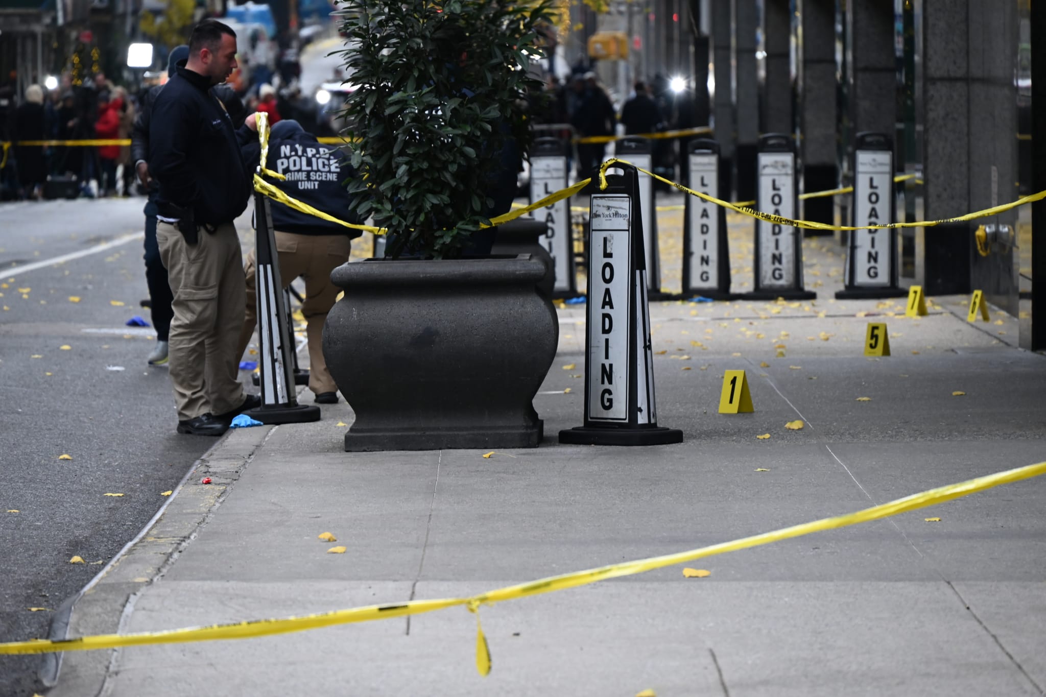 Police officers at a crime scene on a city sidewalk, marked with yellow tape and evidence markers.