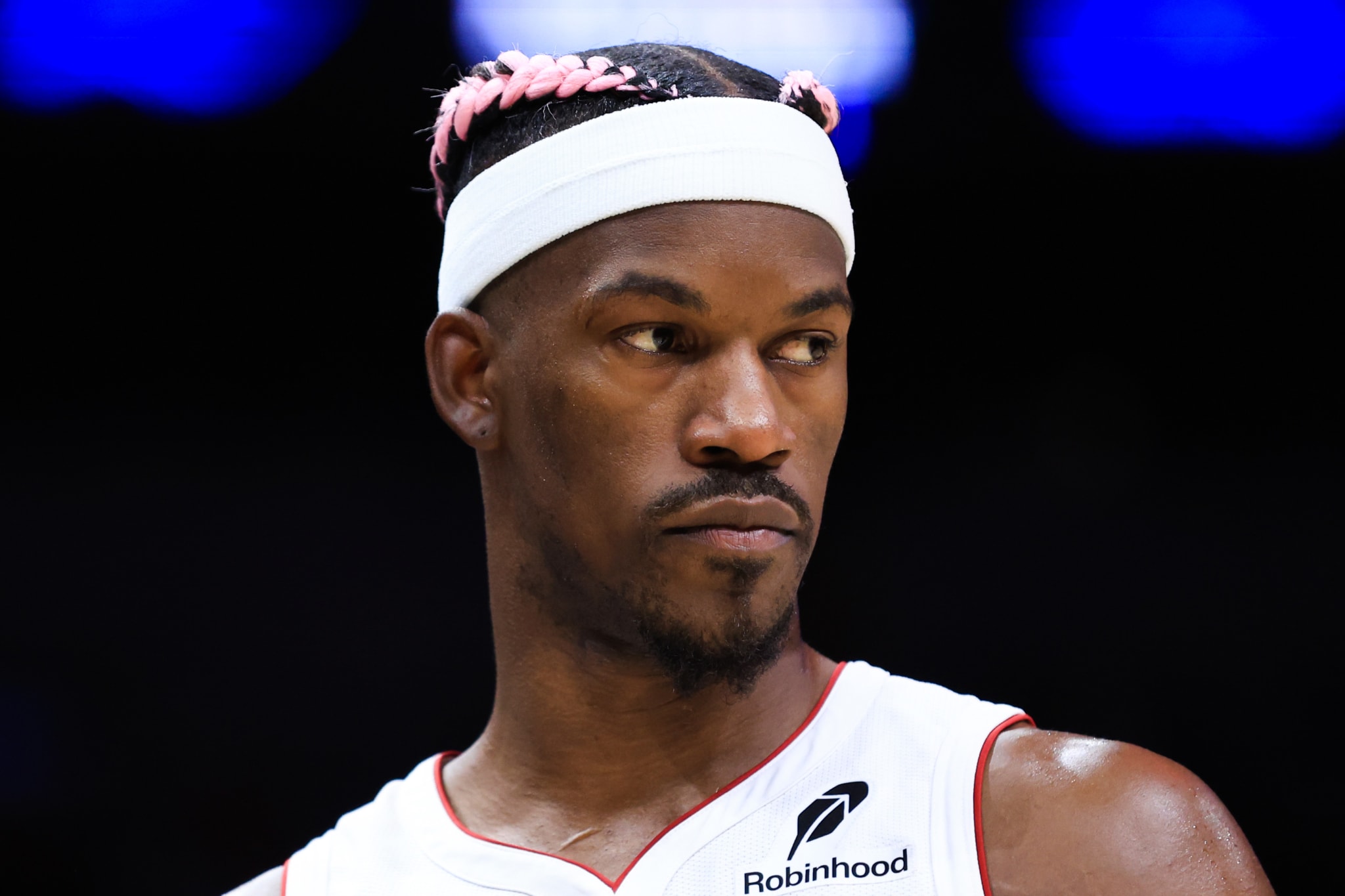 Jimmy Butler, wearing a white headband and a Miami Heat jersey, looks to the side with a serious expression.