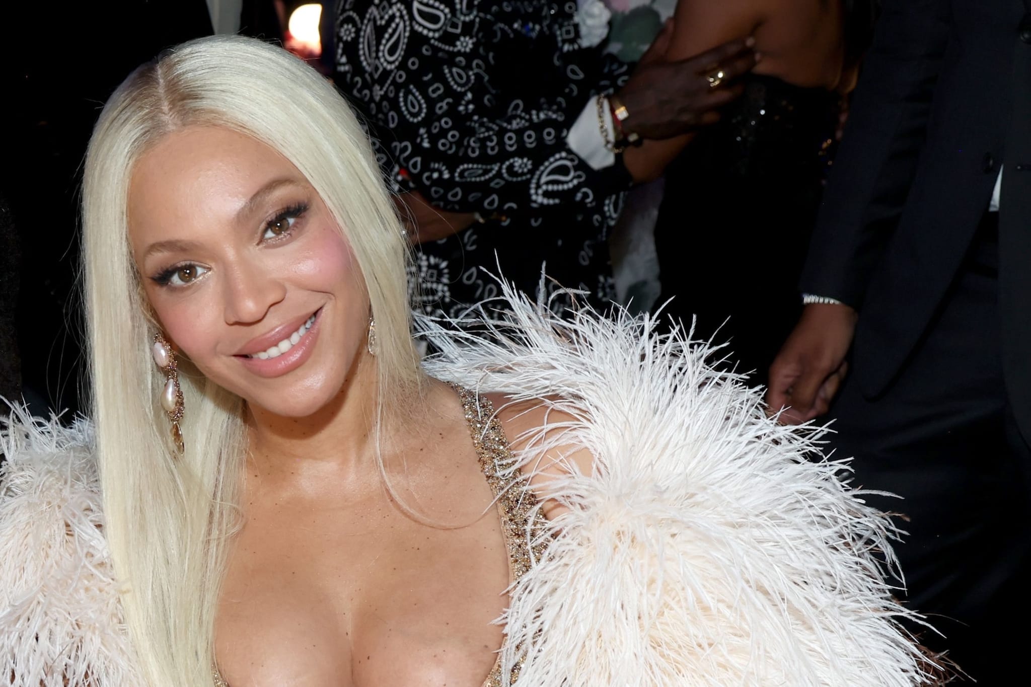 Beyoncé smiling at an event, wearing a glamorous outfit with a feathered detail.