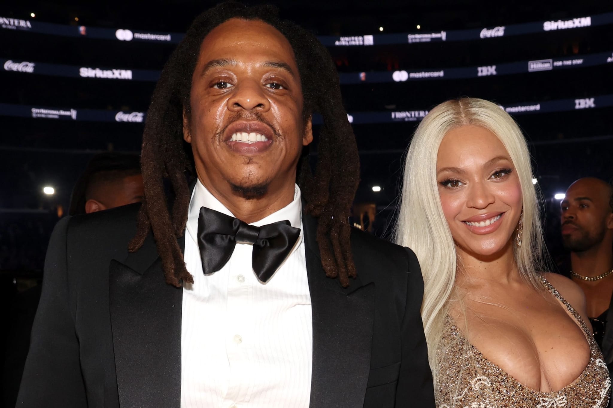 Jay-Z and Beyoncé smiling at an event. Jay-Z is in a tuxedo, and Beyoncé is wearing a sparkling dress.