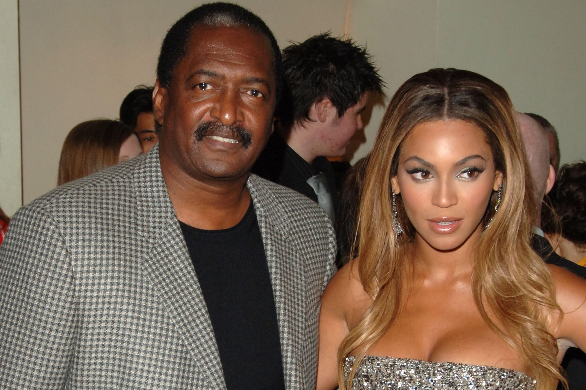 Mathew Knowles in a checkered blazer stands beside Beyoncé, who is wearing a sparkly strapless dress.
