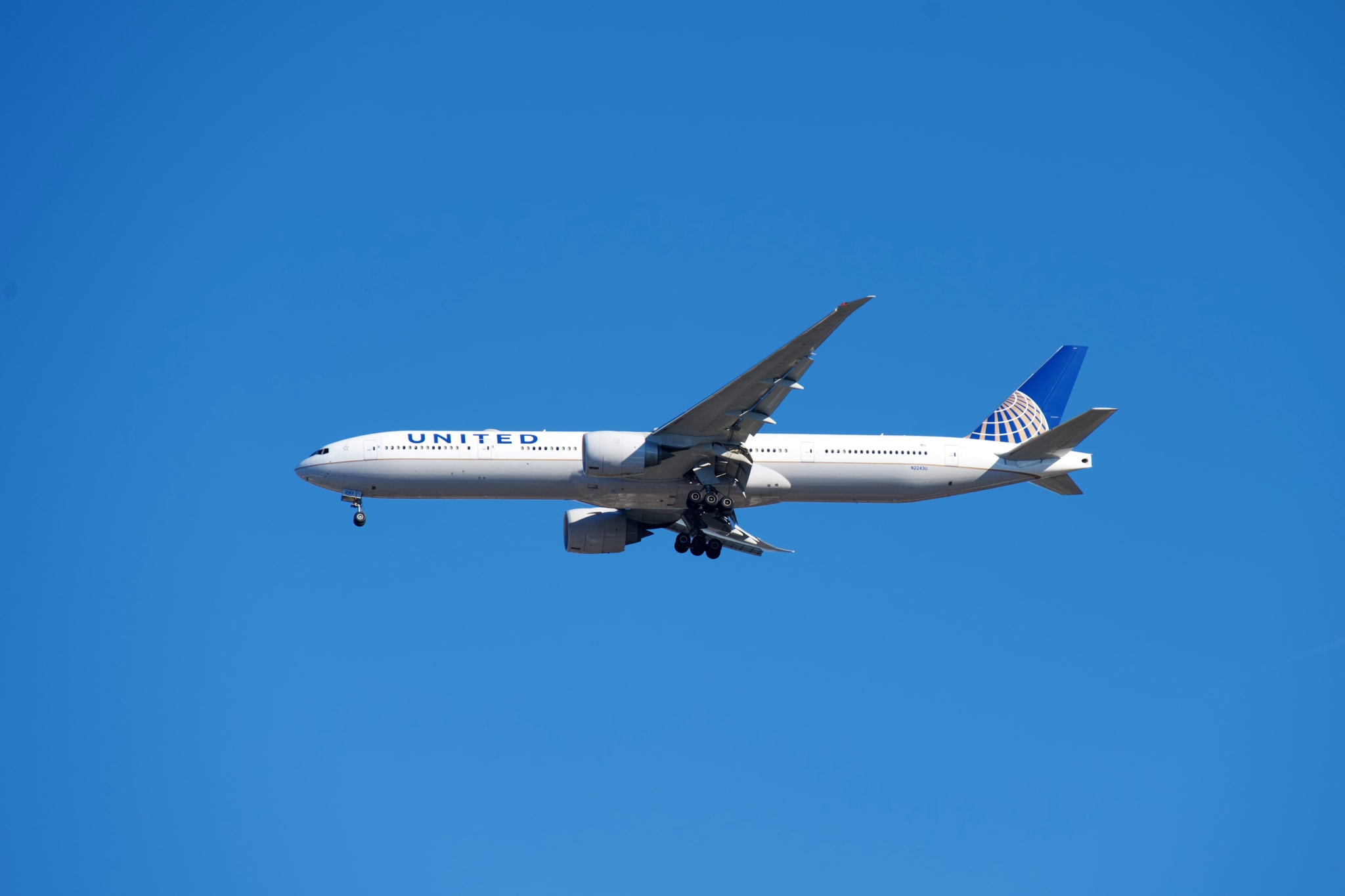 A United Airlines airplane flying against a clear blue sky.