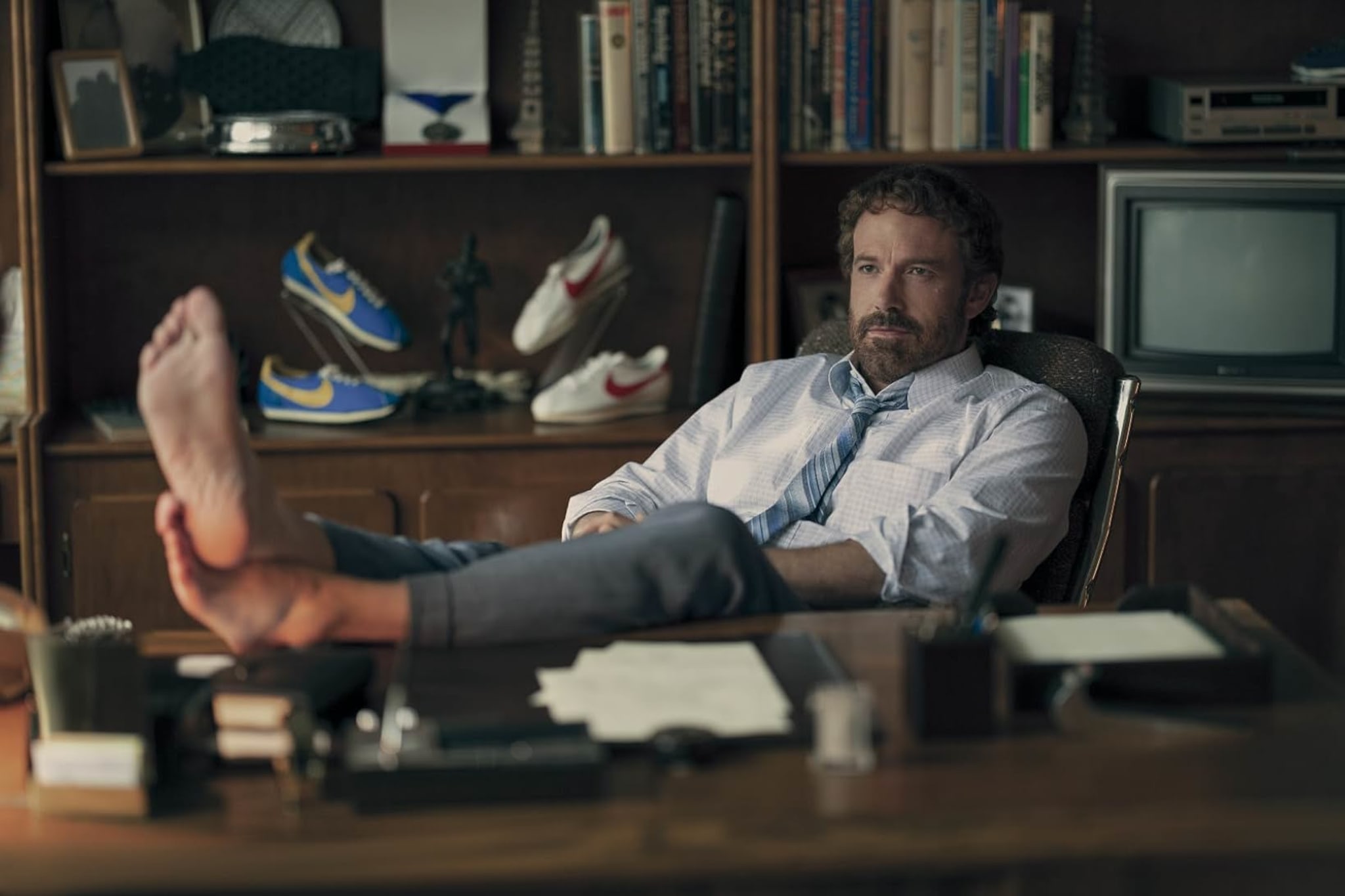 A man in an office with feet up on a desk, surrounded by books and vintage Nike shoes.
