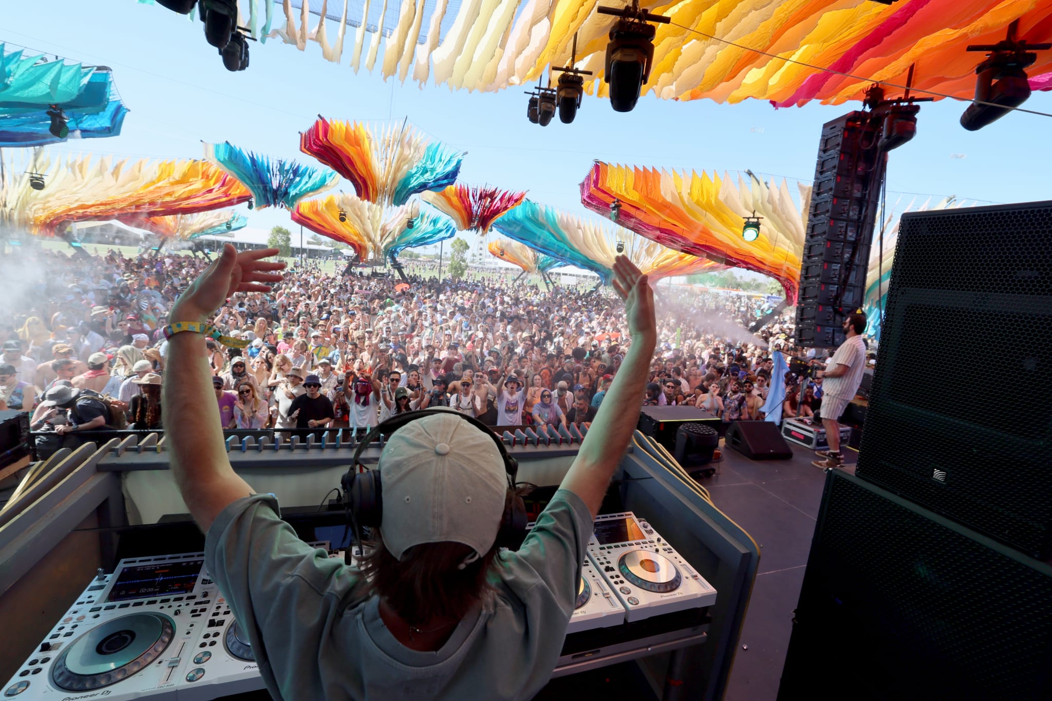 DJ performing on stage at Coachella 2025, colorful decorations above, and a large crowd enjoying the music.