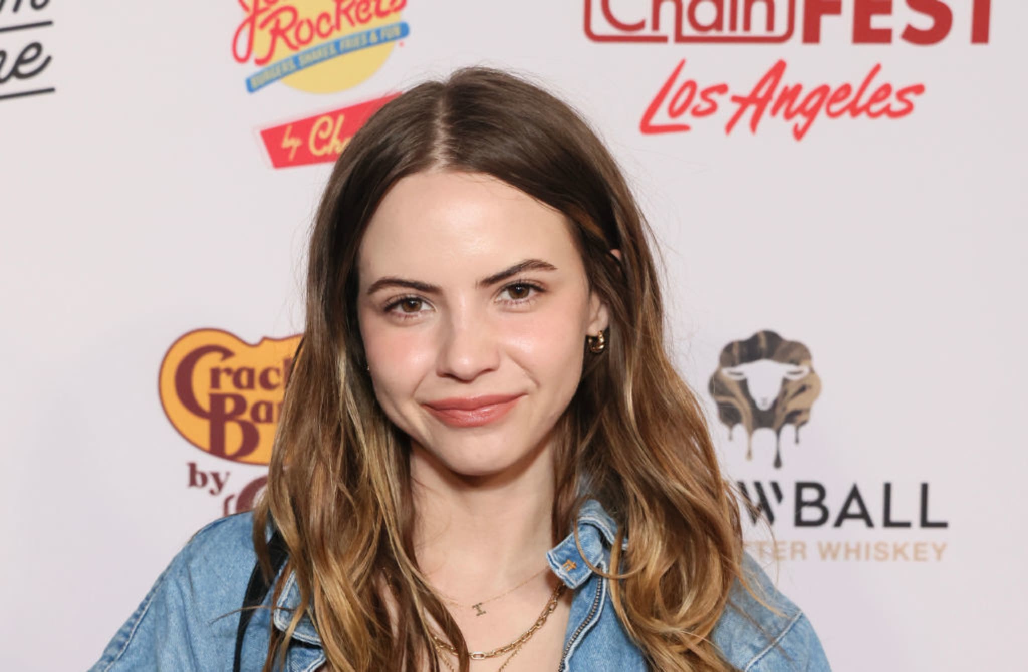 A woman with long brown hair smiles at an event, wearing a denim jacket. The background has logos for Chain Fest and Cracker Barrel.