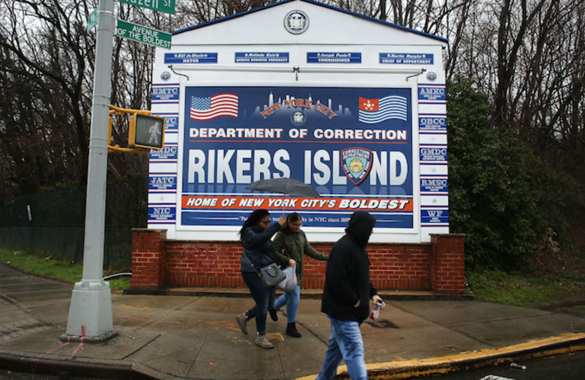 People walk by a sign at the entrance to Rikers Island