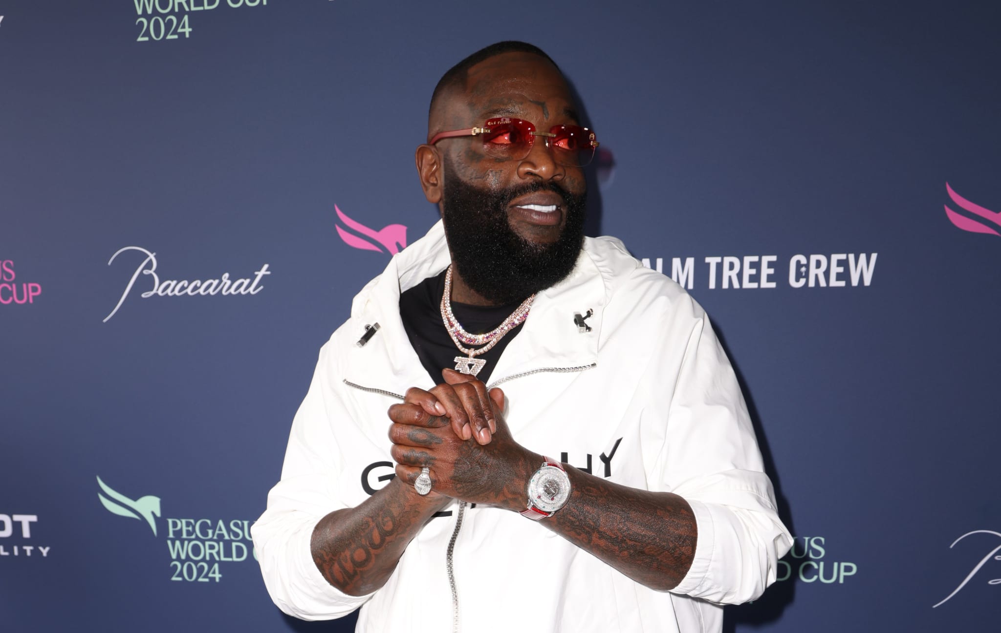 Rick Ross in a white jacket with accessories, posing at an event