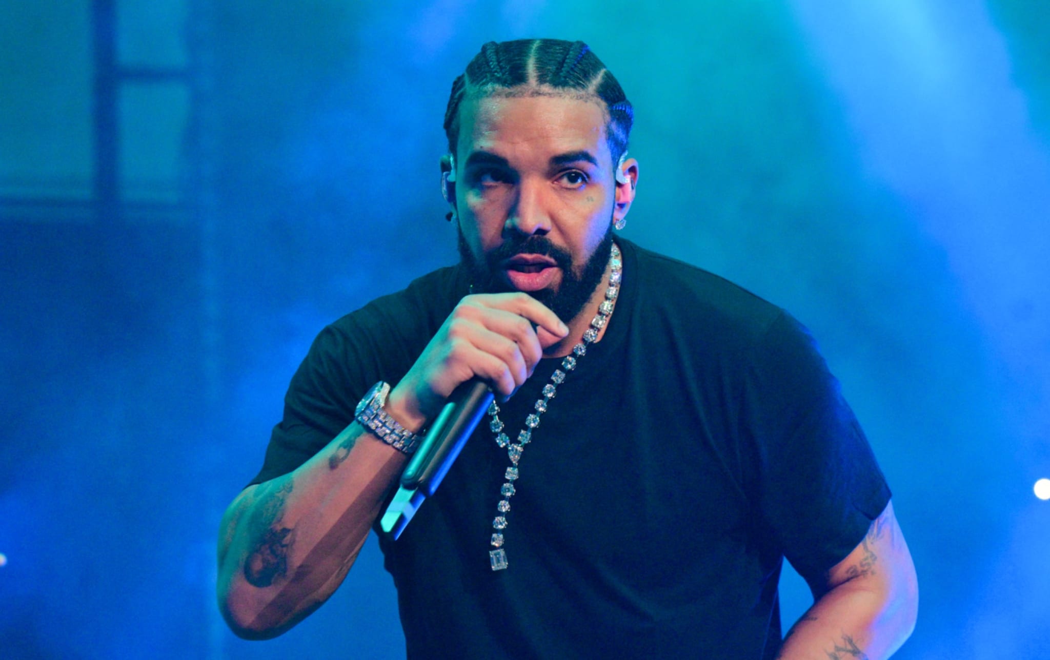 Drake performs on stage, wearing a black t-shirt and pants, with a microphone in hand