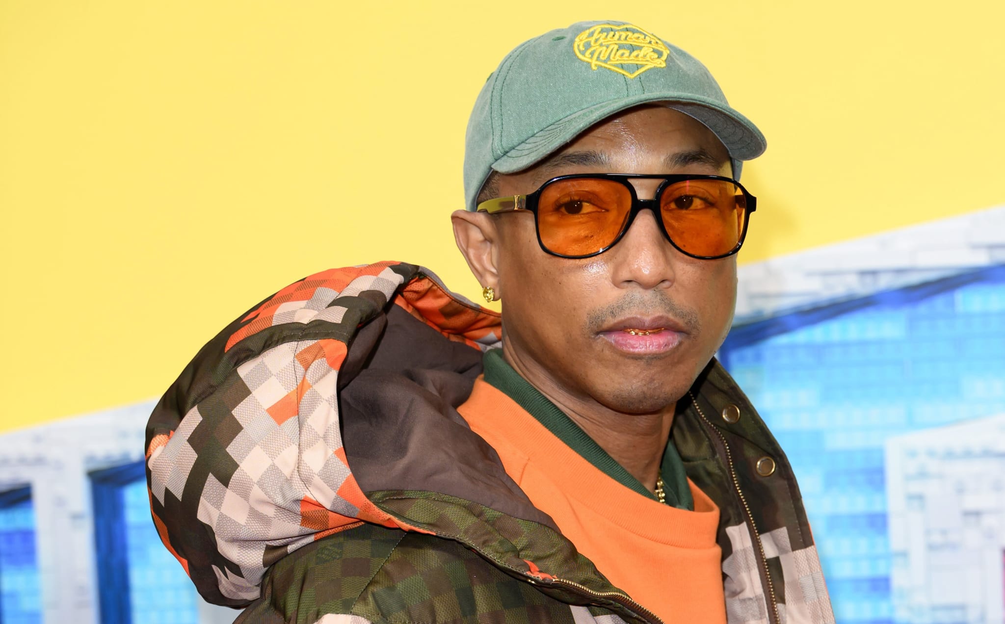 Pharrell Williams wears cap, sunglasses, and orange checkered coat. 